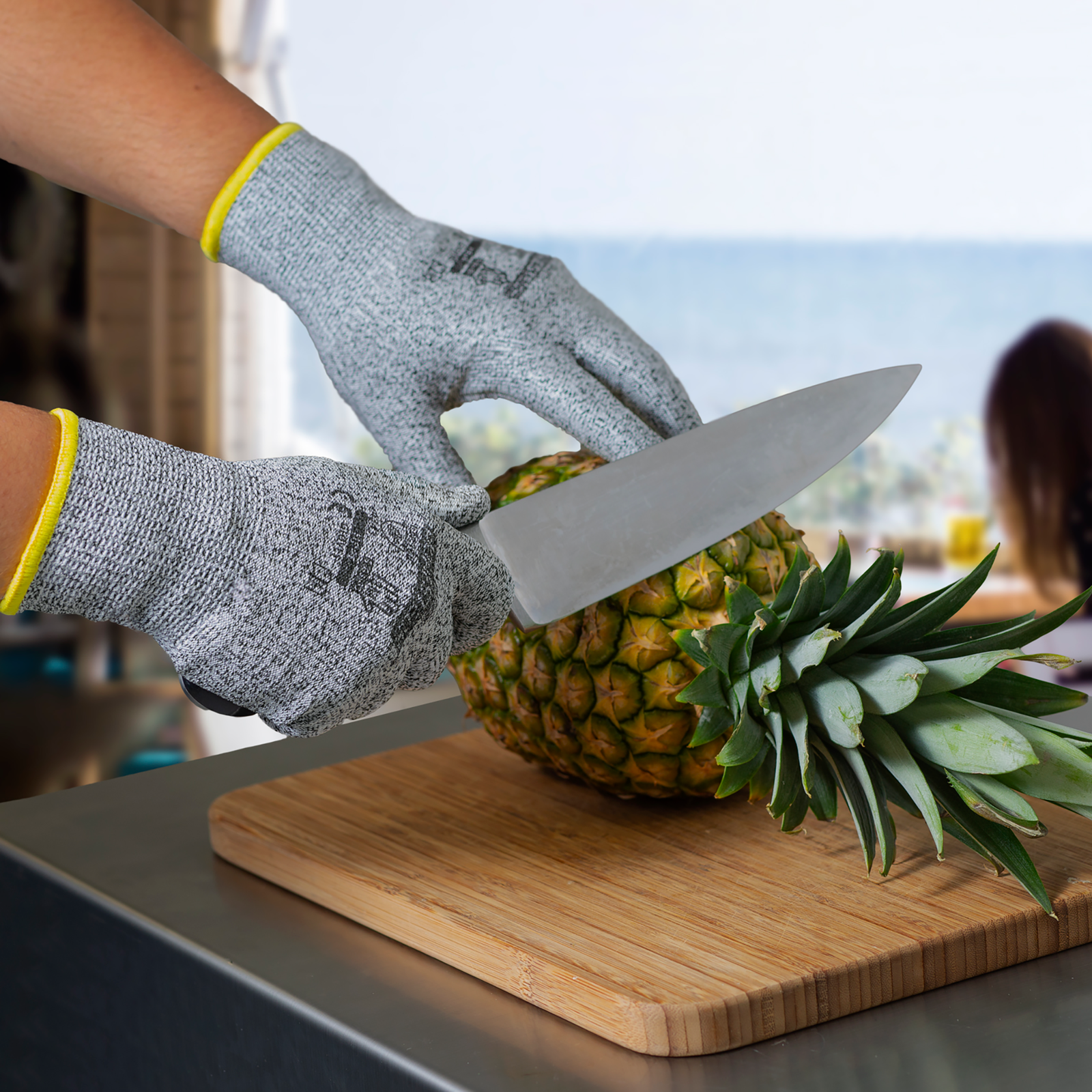 Person wearing the Jorestech multi purpose safety work glove while holding a chefs knife to cut the crown of a pineapple