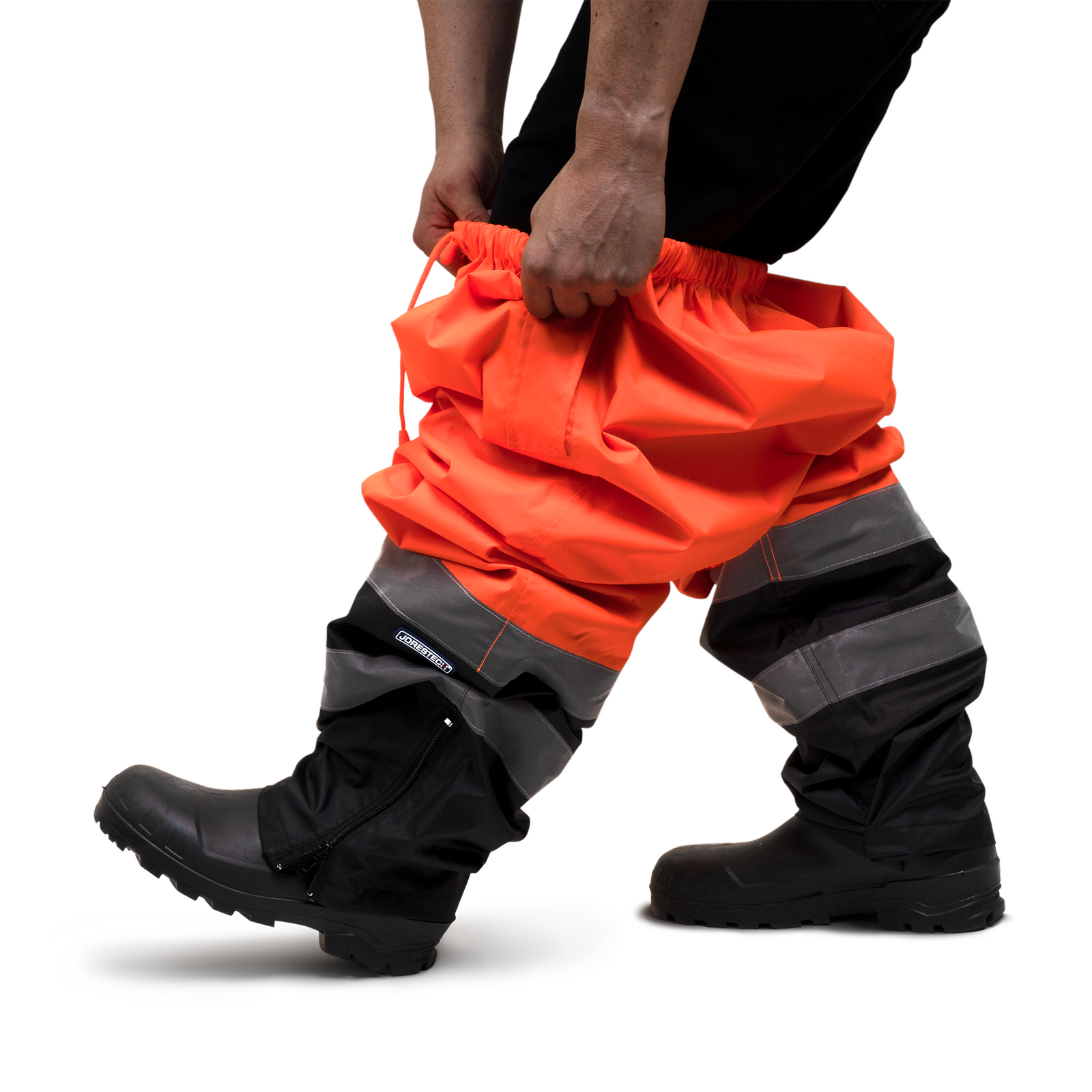 A person putting on the JORESTECH orange and black safety rain pants as a rain protection layer on top of his own clothing