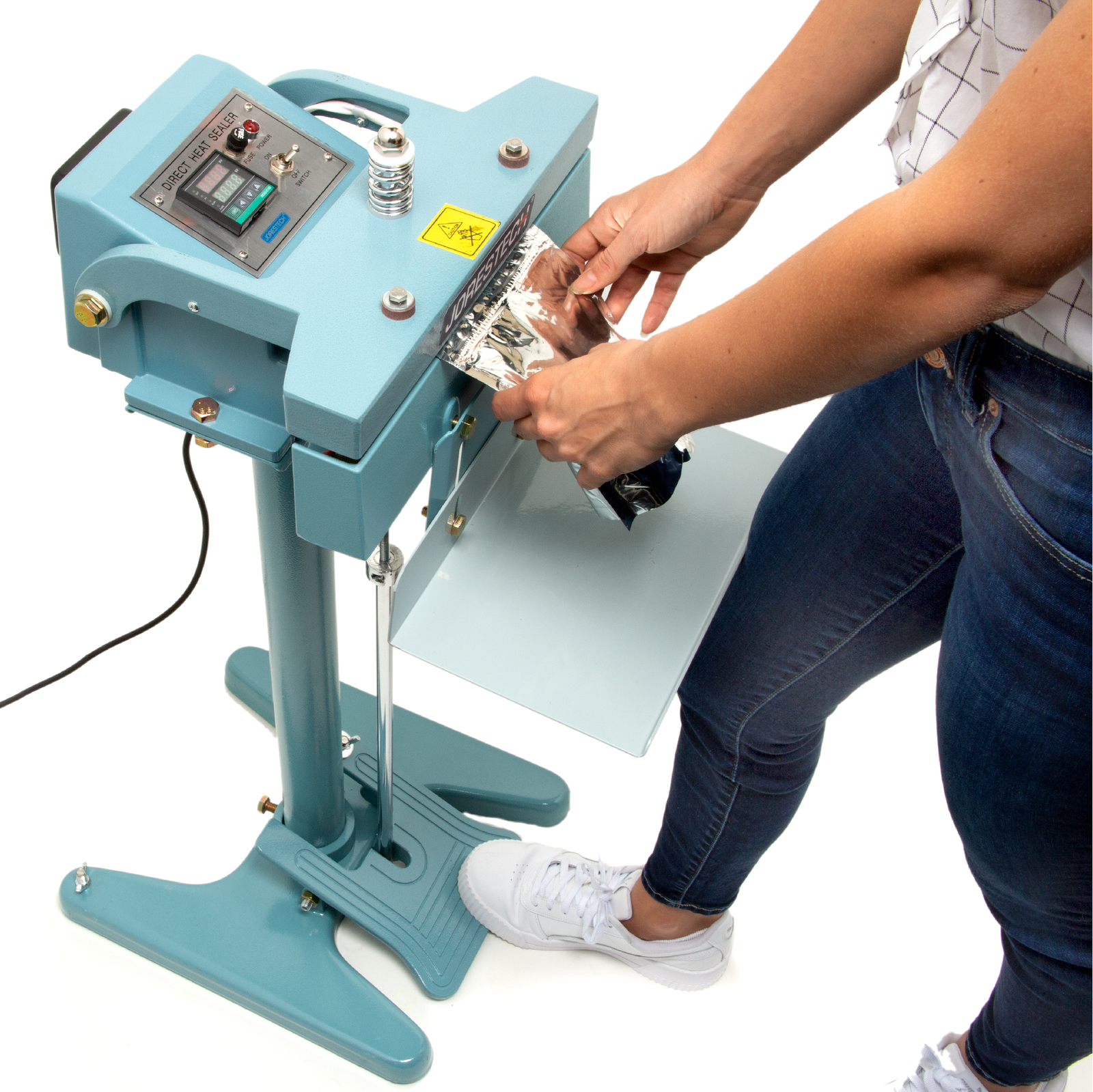 Woman stepping on the foot pedal of the blue JORES TECHNOLOGIES® constant impulse bag sealer. She is sealing a silver plastic pouch bag.