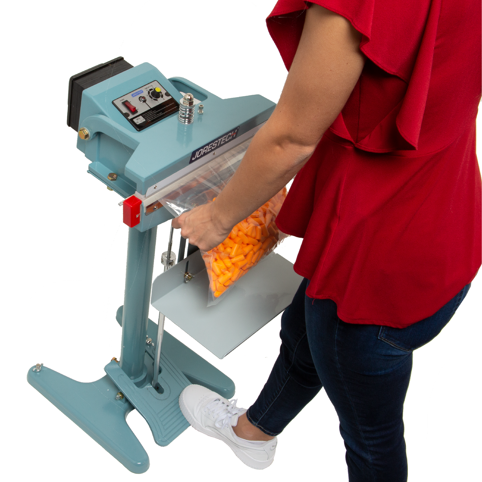 A person wearing a red shirt and jeans. She is sealing a large bag filled with earplugs using the 18 inch foot impulse bag sealer