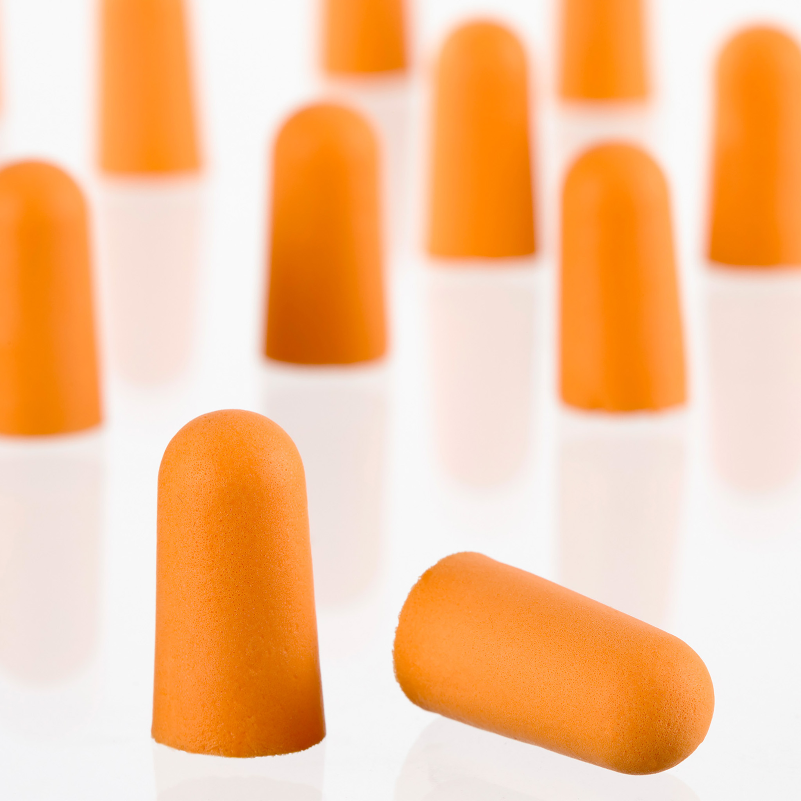 Close up show in detail the soft orange foam of 2 ear plugs. many additional ear plugs can be seen in the background