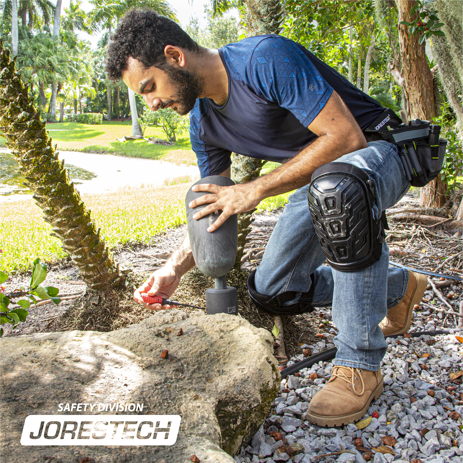 An electrician wearing JORESTECH gel filled knee pads, kneeling on rocks while fixing a garden light