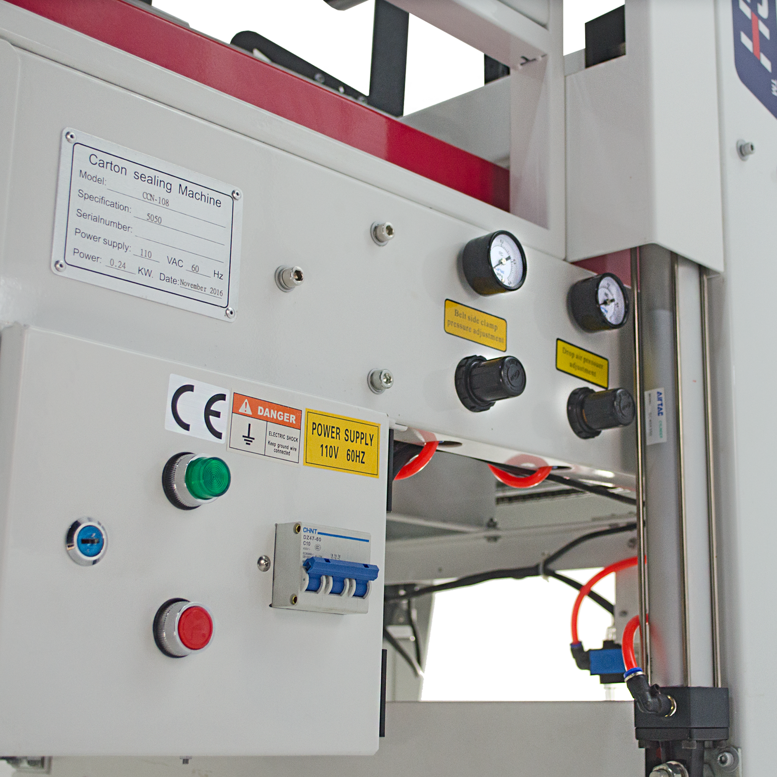Close up of an automatic case sealer machine control panel with black adjusting knobs, green on indicator light and red emergency stop button.