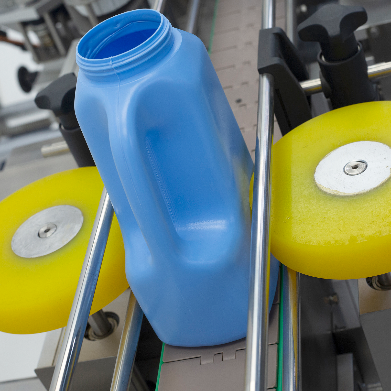 Stainless steel dual automatic label applicator with blue plastic oval containers placed on the conveyor. Machine is placing the stickers on one side of the blue containers.