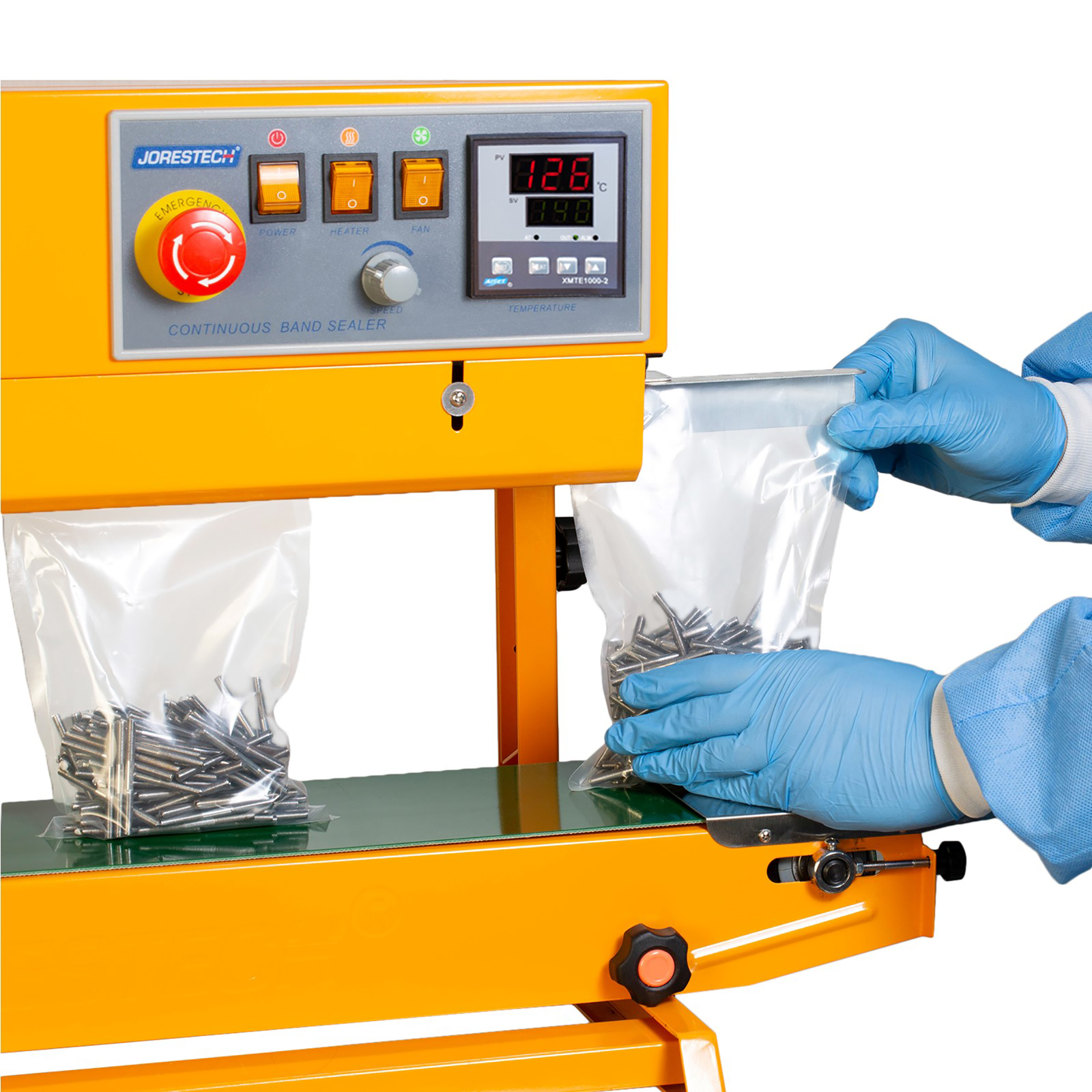 An operator wearing blue gloves and disposable clothing inserting plastic bags filled with nails into the yellow JORES TECHNOLOGIES® continuous band sealer. The bag sealer positioned for vertical applications