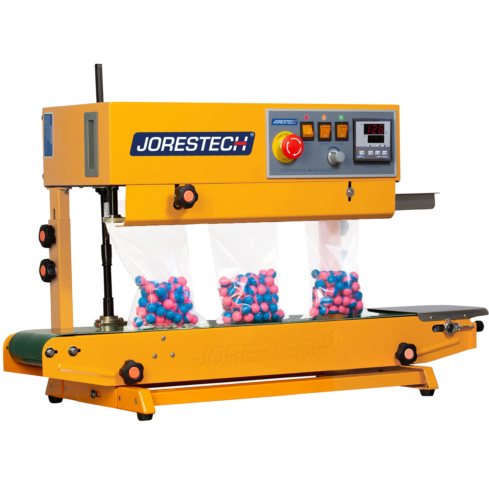 Diagonal view of the yellow JORES TECHNOLOGIES® horizontal continuous band sealer shown sealing 3 clear sealable bags filled with pink and blue paint balls.  Control panel can also be seen with digital temperature control, the red emergency stop button and other switches