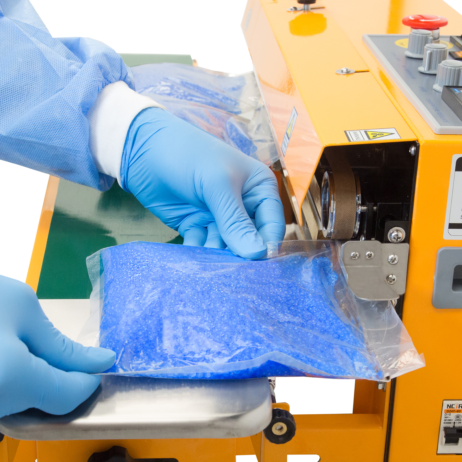 operator wearing blue gloves inserting a plastic bag filled with blue wax beads into a JORES TECHNOLOGIES® horizontal and vertical continuous band sealer . The bag sealer positioned for horizontal applications