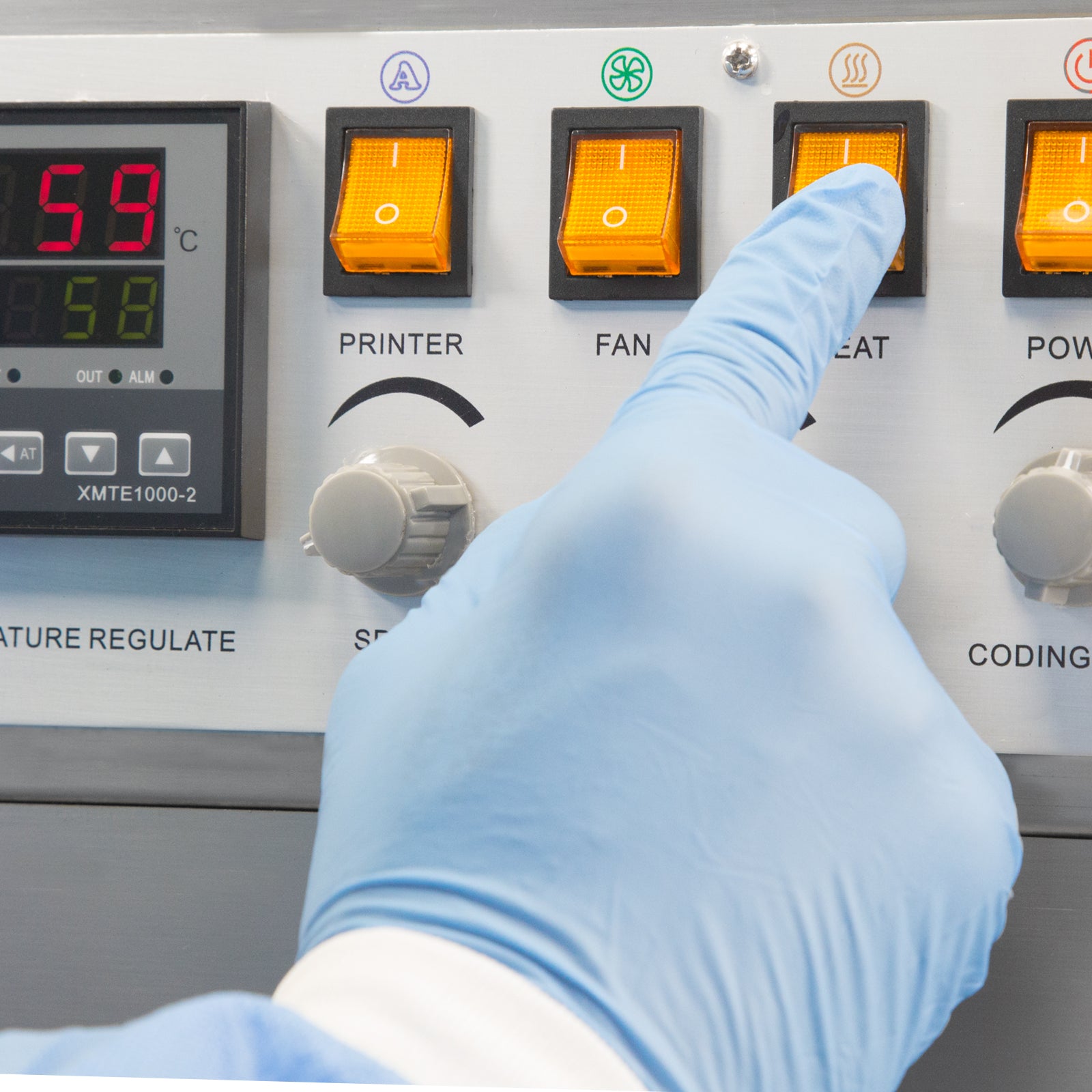 Close up showing the control panel of a JORES TECHNOLOGIES® continuous band sealer and the hand of a person pressing an orange switch to set the bag sealer to start sealing plastic bags.