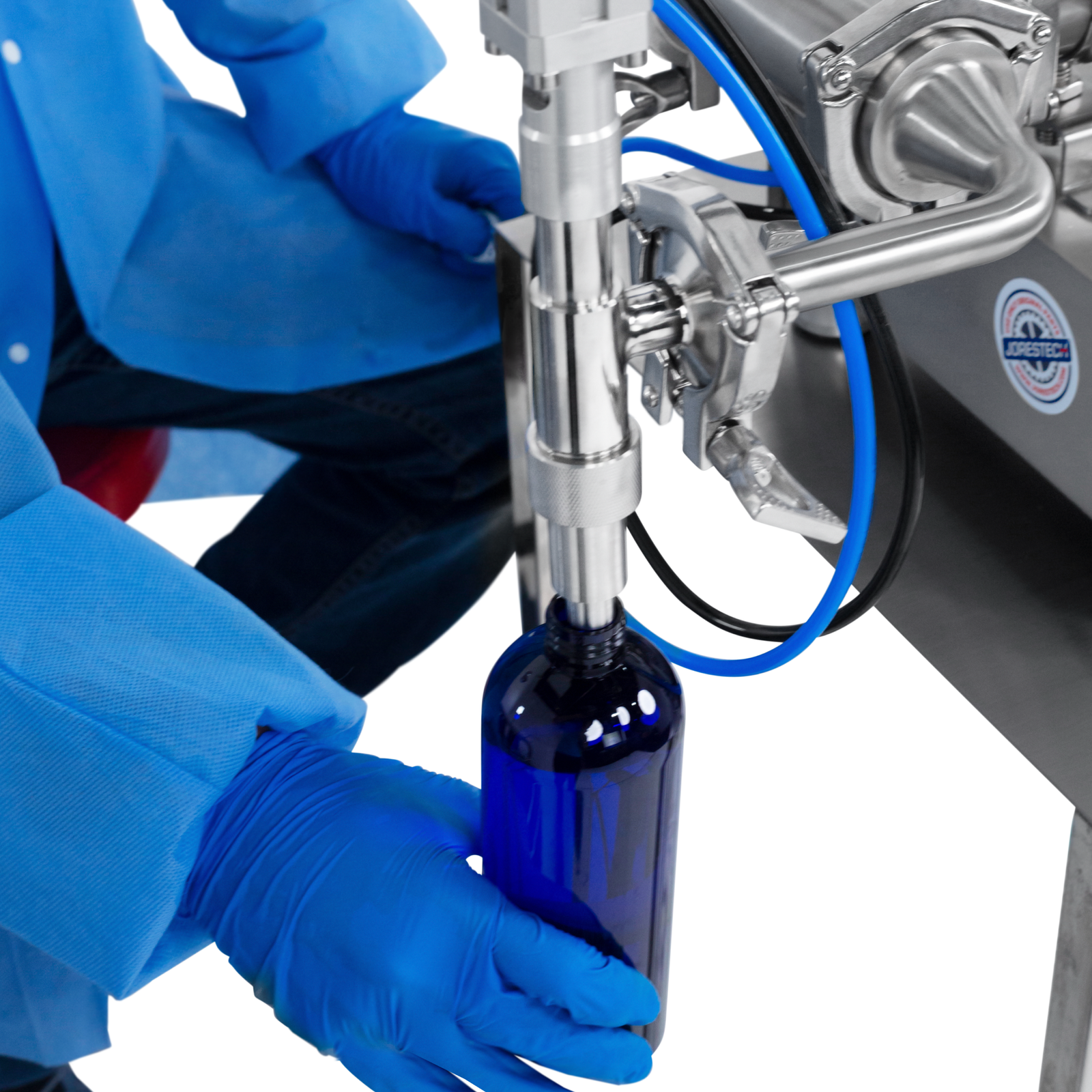 A worker wearing nitrile safety gloves operating the JORES TECHNOLOGIES® Low Viscosity Piston Filler. The person is positioning a 500ml bottle below the tip of the non-drip nozzle to be filled with accuracy by the liquid filling machine