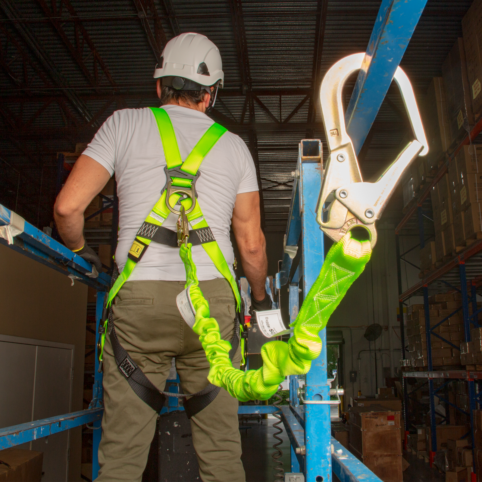A worker wearing the lime JORESTECH single leg internal shock absorbing lanyard with snap hook and scaffolding. The person has the lanyard attached to D ring of a harness and to the metal frame of a lift