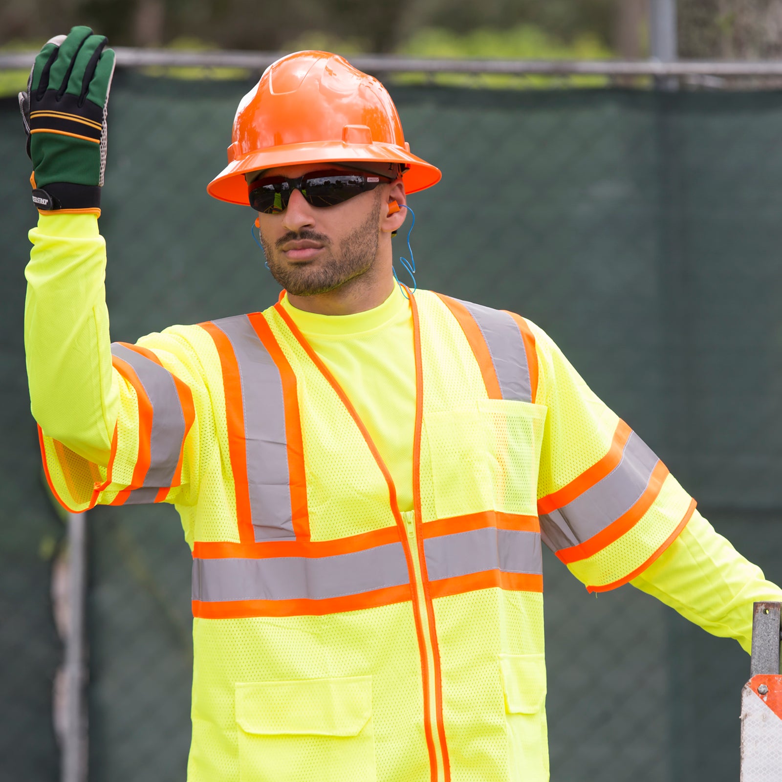 A worker directing traffic wearing yellow high visibility reflective clothing, an orange hard hat and the JORESTECH smoke safety glasses for high impact protection during a road construction.