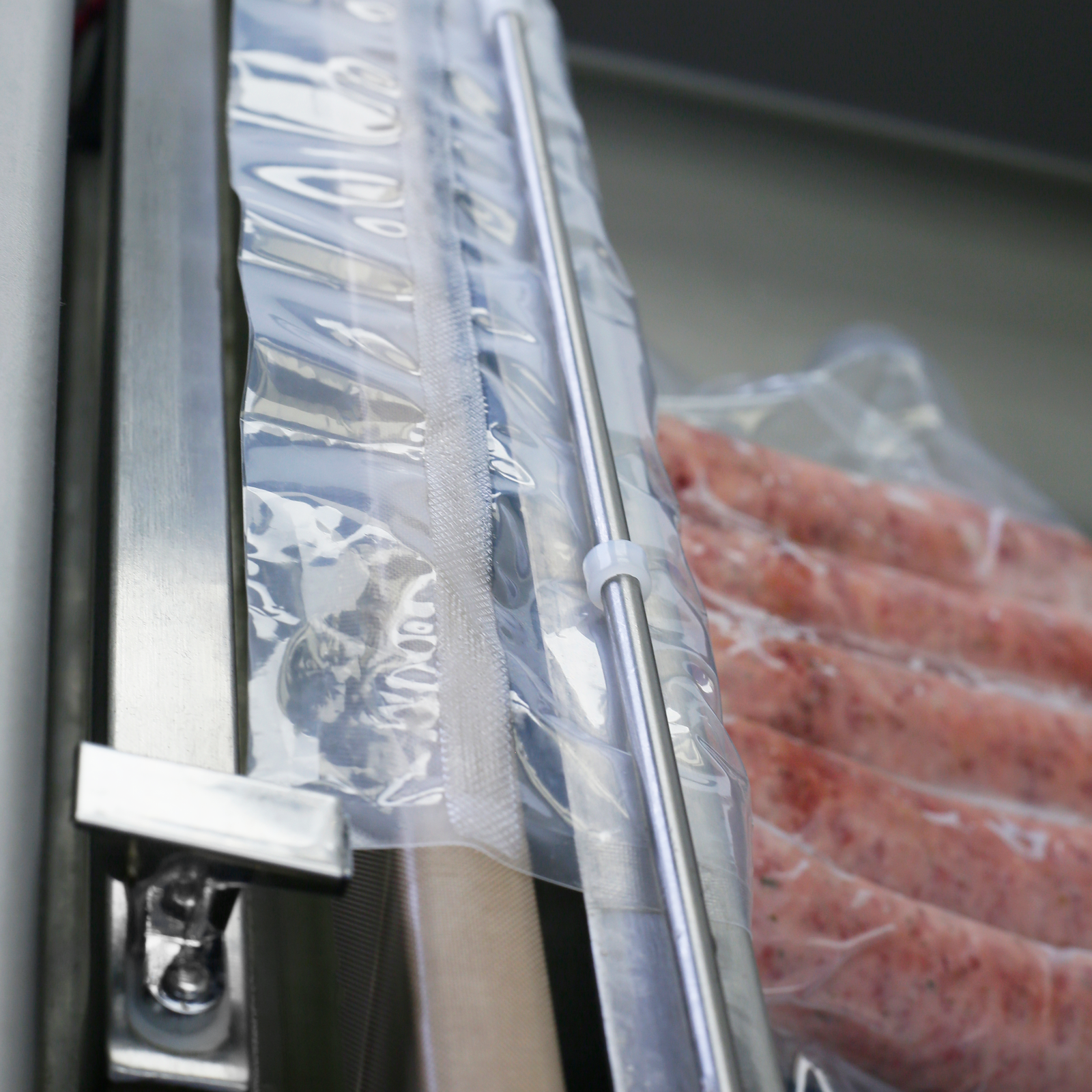 close-up of the vacuum sealer's heating element, the vacuum bag holding bar, and a fresh seal on a plastic bag that is laying on top of the sealing element to begin the process of sealing meat in a bag