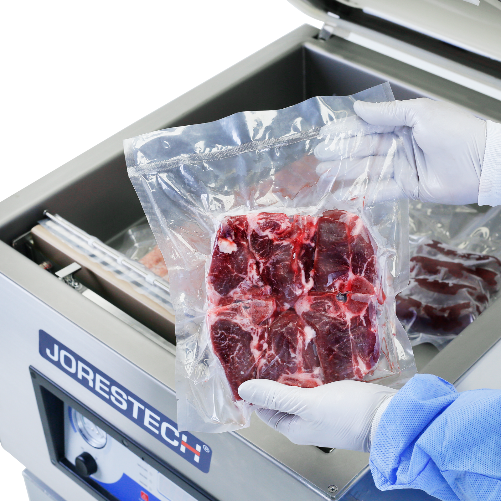 Operator wearing a blue PPE gown and latex gloves holding a package with freshly sealed red meat over the JORES TECHNOLOGIES® Tabletop commercial vacuum sealer