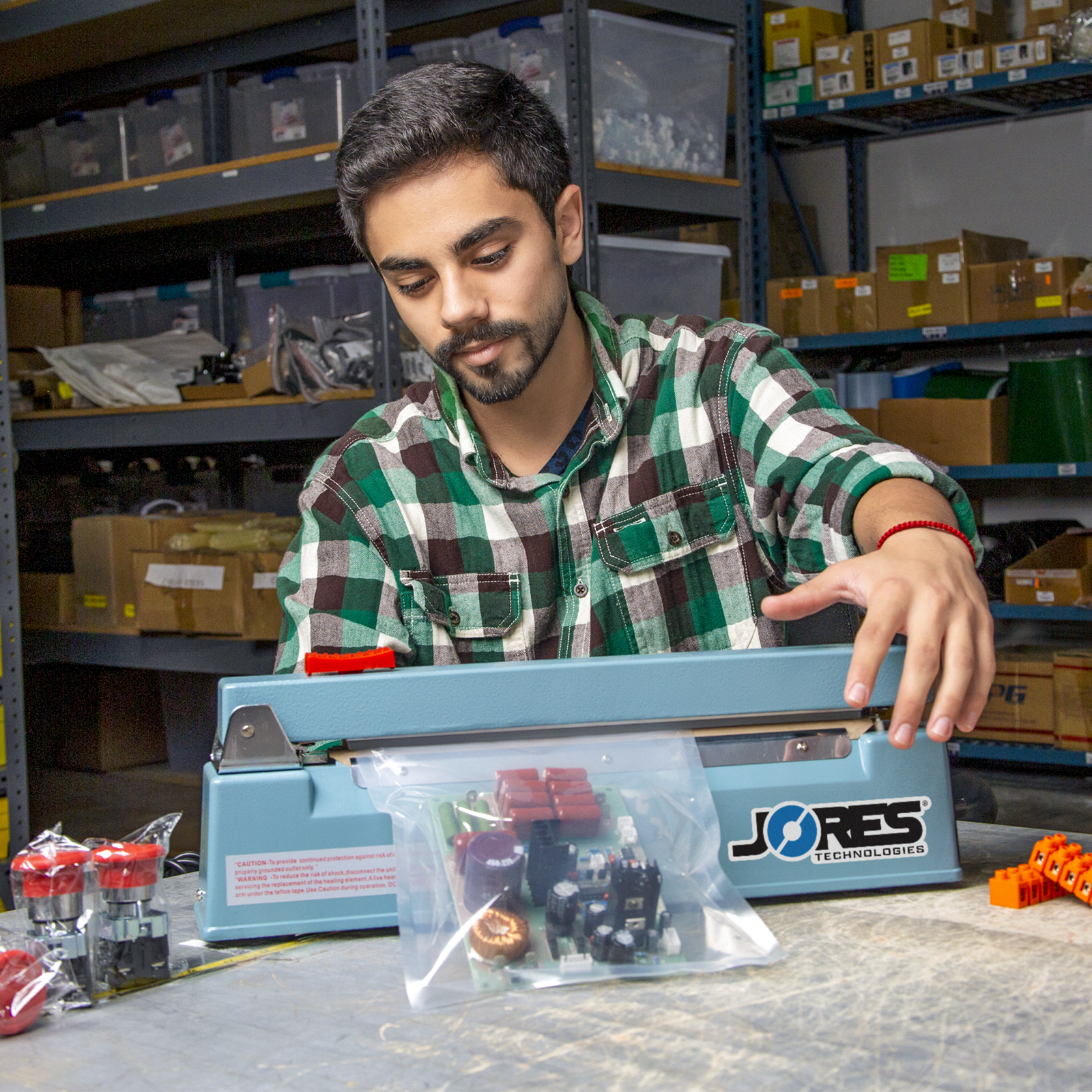 Worker in a tech warehouse setting sealing a heat sealable bag with the 12 inch  manual impulse bag sealer with cutter