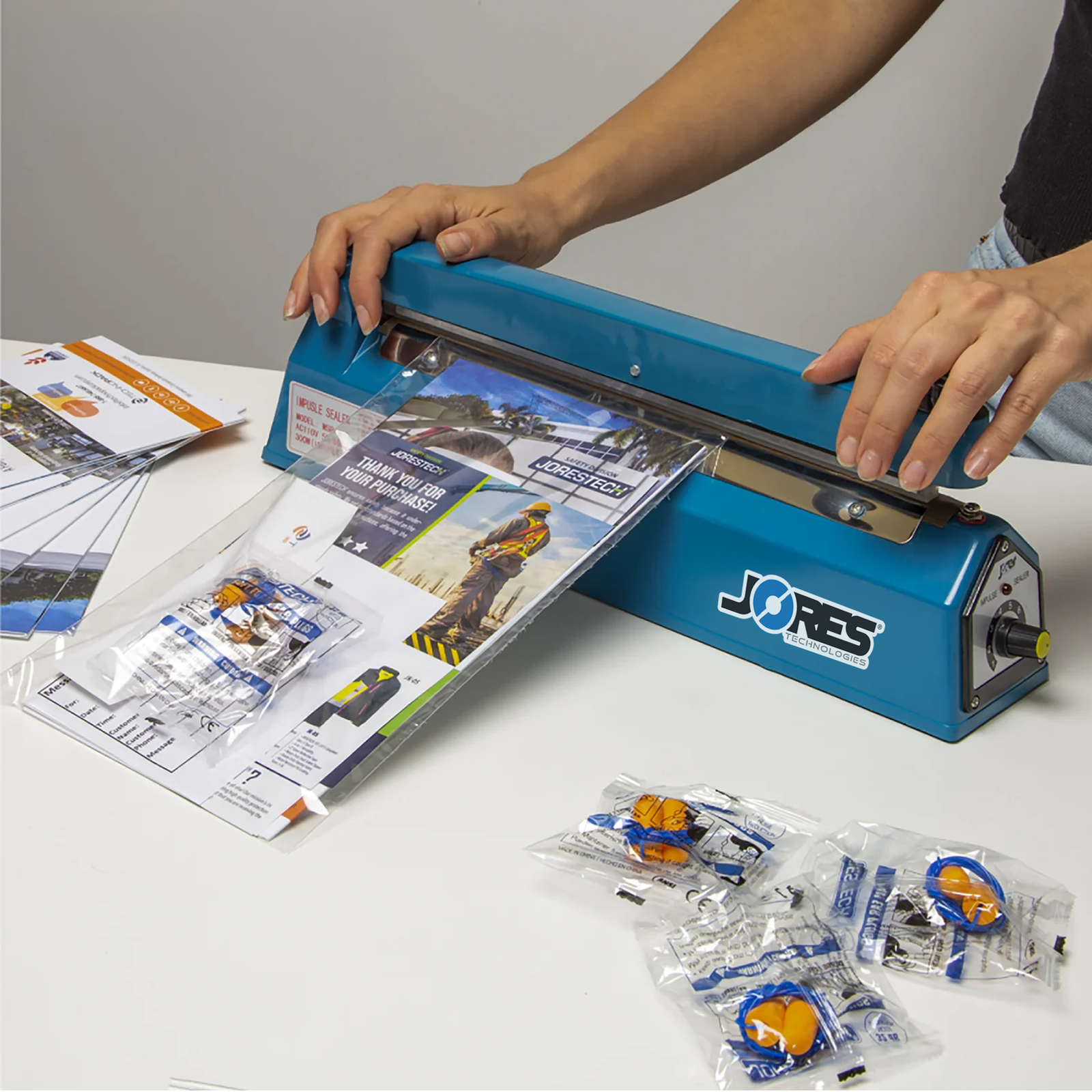 Person using the 12 inch manual impulse sealer to close a bags with a promotional packet bundle inside. 