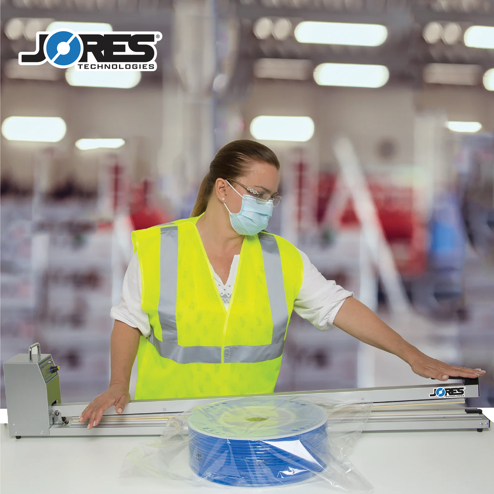 Woman in a factory setting wearing PPE sealing a bag containing a large roll of blue cable with a JORES TECHNOLOGIES® Extra Long Manual Impulse Bag Sealer.