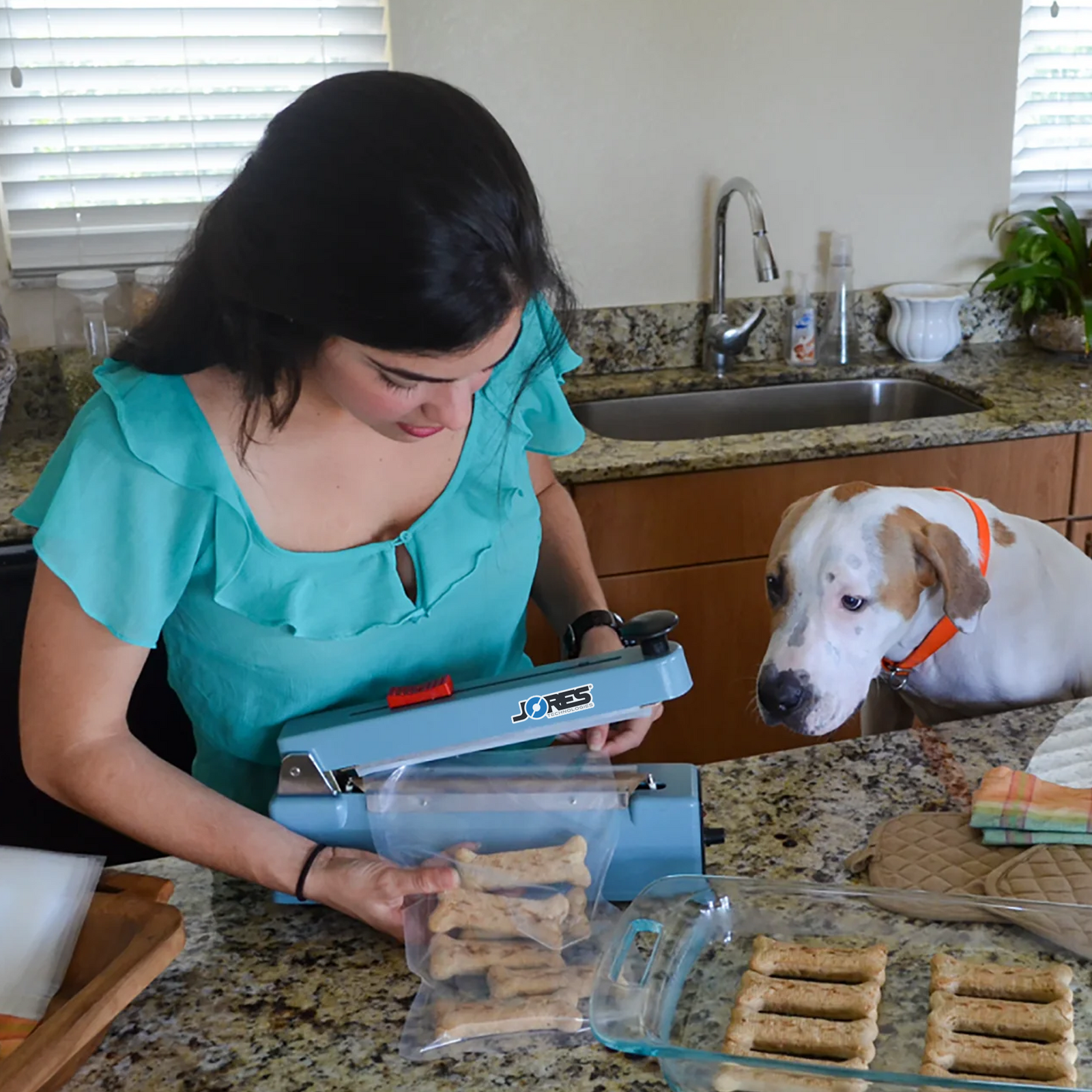 Woman and her dog in their kitchen. she is packaging Dog treats in sealable bags with the JORES TECHNOLOGIES® 8 inch manual impulse sealer.