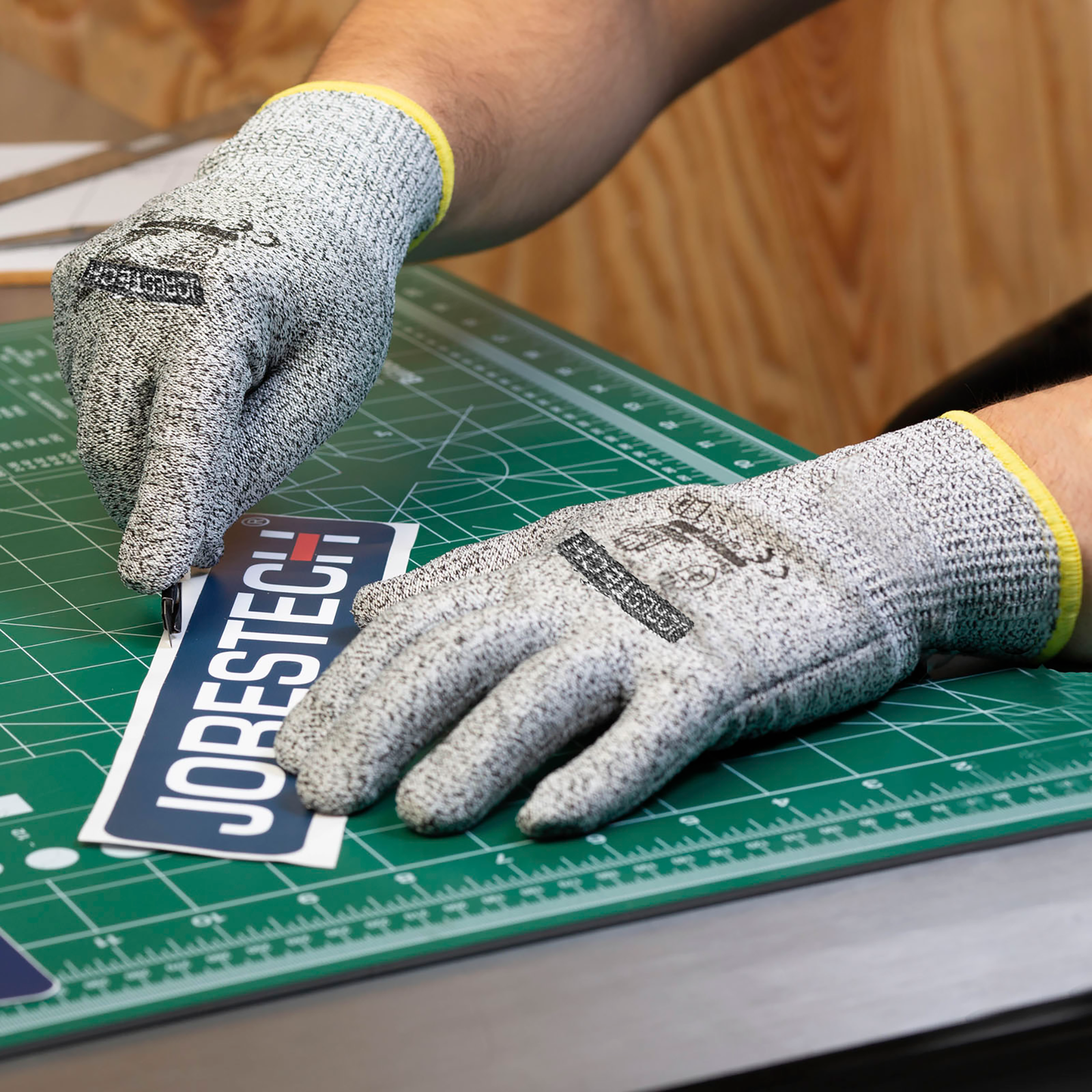 Worker wearing the Jorestech multi purpose safety work glove while cutting a piece of paper with an exact knife