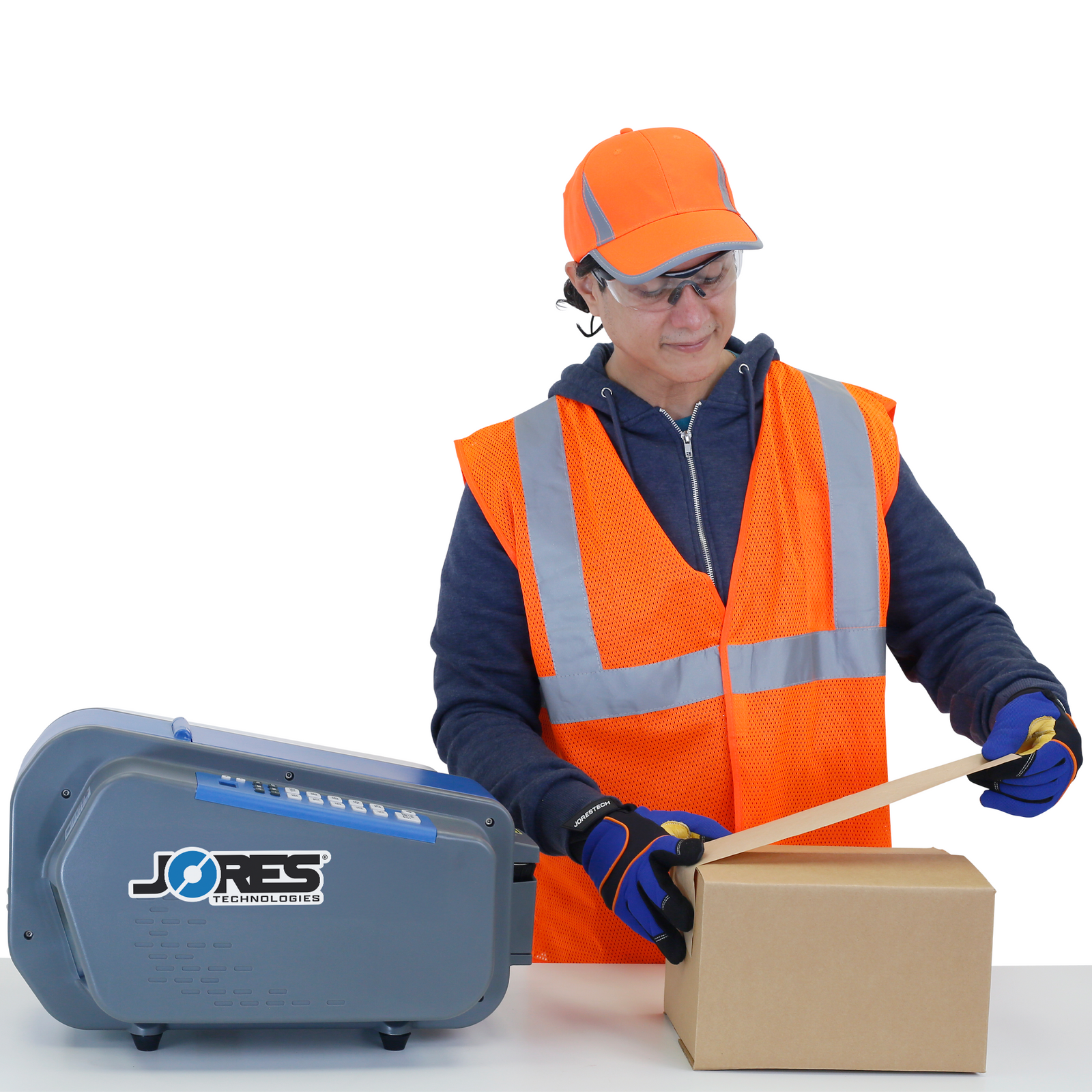 A worker closing boxes using the JORES TECHNOLOGIES® gummed paper tape dispenser. The table top tape dispenser is on top of a working table together with the box being closed. The background is full of brown carton boxes closed with gummed tape