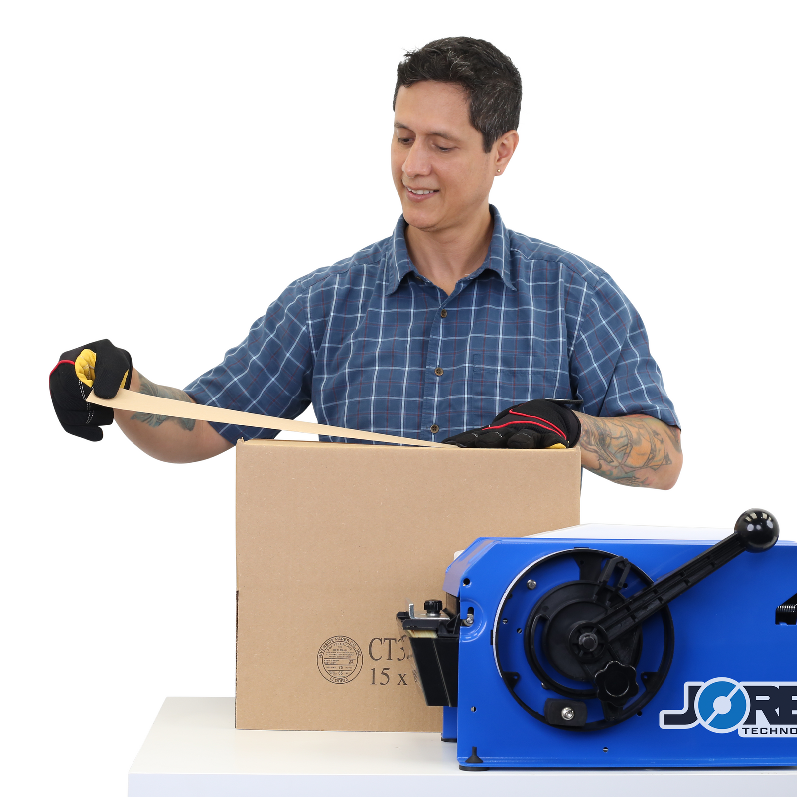 Man placing the wet gummed craft tape on to a brown card box after it was dispensed by the blue JORES TECHNOLOGIES® paper tape dispenser place on the same working table