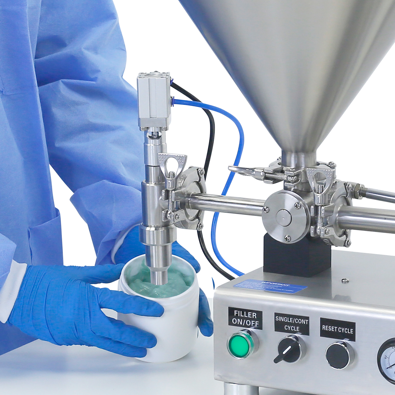 Worker wearing PPE clothing standing in front of the nozzle of a Piston filler. He is removing a container of 100 ml full of a blue viscos gel after been filled by the stainless steel  piston filler that is placed on top of a working table