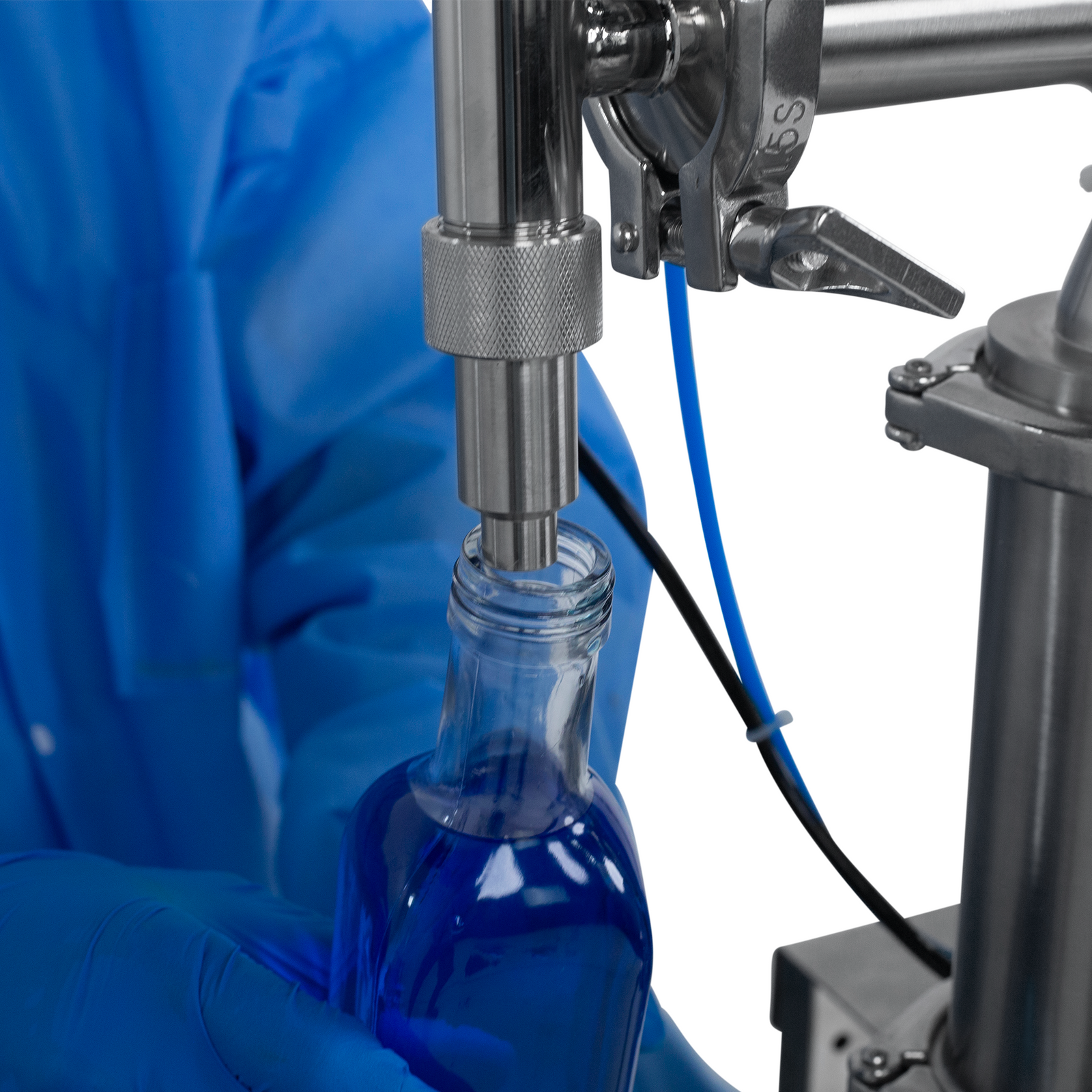 Worker wearing nitrile safety gloves operating the JORES TECHNOLOGIES® Low Viscosity Piston Filler for 1000ml bottles. The person is positioning a 1000ml bottle below the tip of the non-drip nozzle to be filled with accuracy by the liquid filling machine.