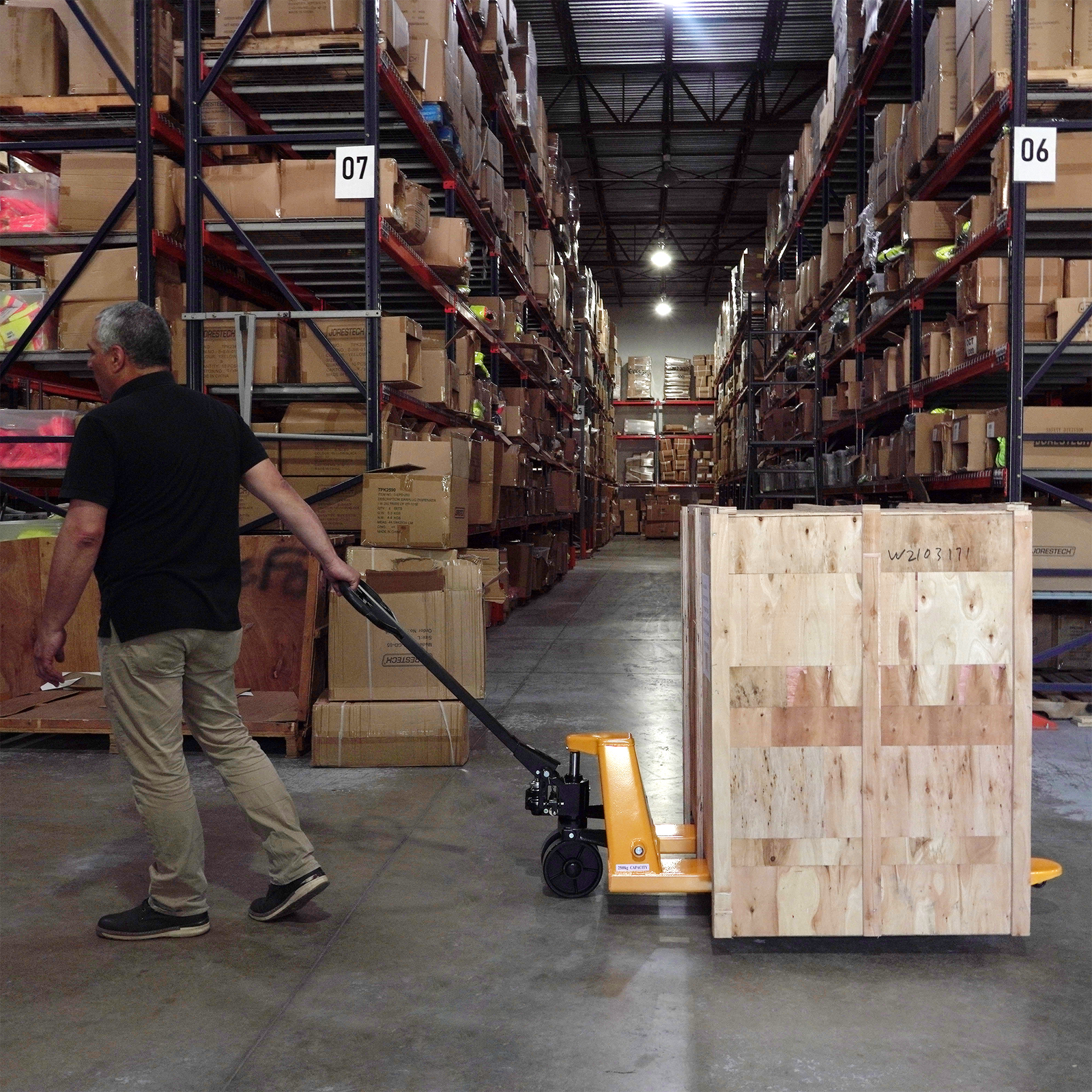 Worker pushing a narrow pallet jack truck with a wooden cate on top