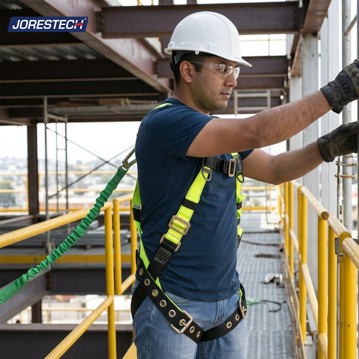 Jorestech S-HARN-02 high-visibility lime-yellow industrial safety harness with grommeted tongue buckle leg straps, attached lanyard, and safety helmet, shown on a male construction worker standing on an elevated outdoor scaffolding catwalk.