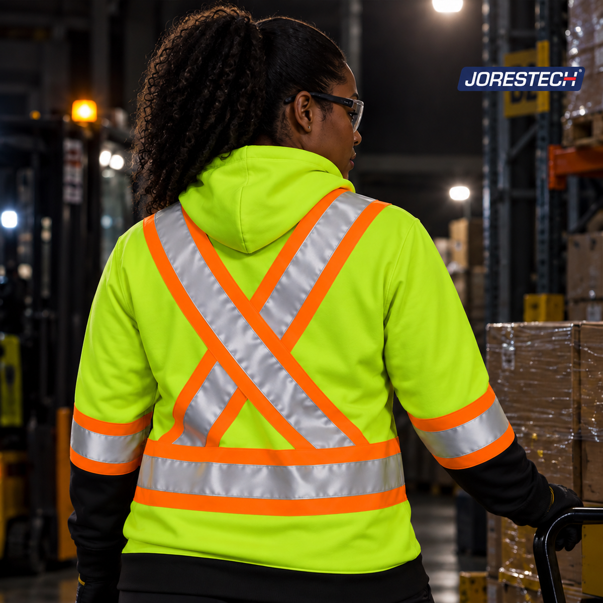 Rear view of a Jorestech high-visibility lime-yellow safety hoodie for women, highlighting the ANSI-compliant X-back reflective stripe design in a warehouse logistics environment.