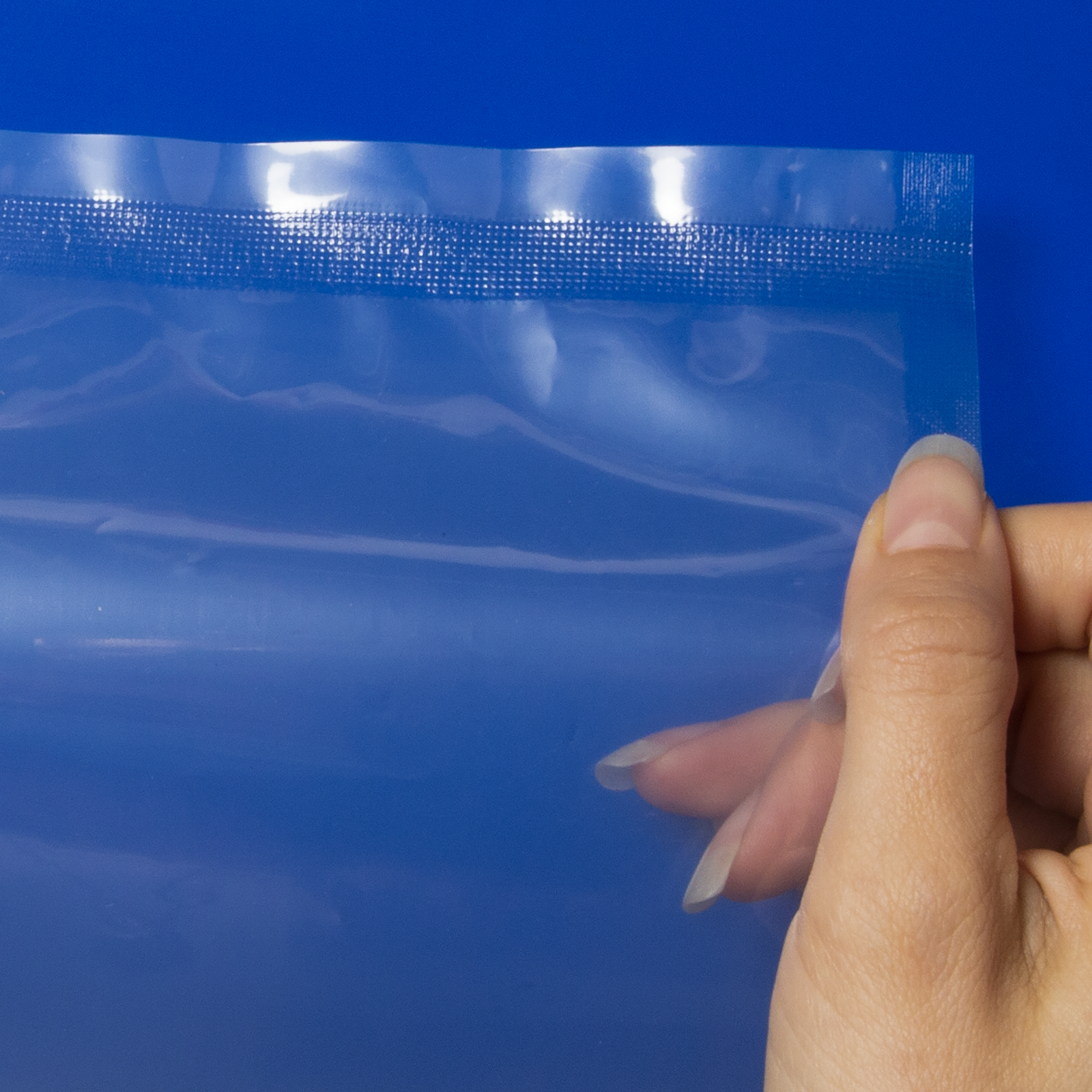 close up of  the hand of a person holding plastic bag sealed by a JORES TECHNOLOGIES® continuous band sealer over a blue background. Detail shows the pattern of the seal.