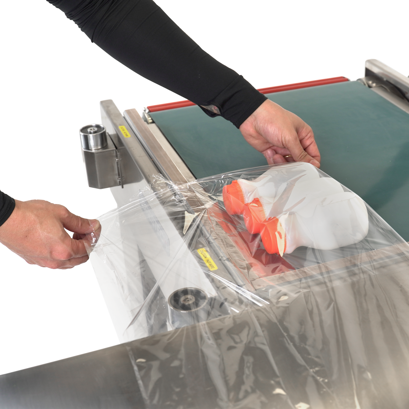 worker using the Stainless steel semi-automatic L bar heat sealer with conveyor to pack bundles of medium size plastic containers.
