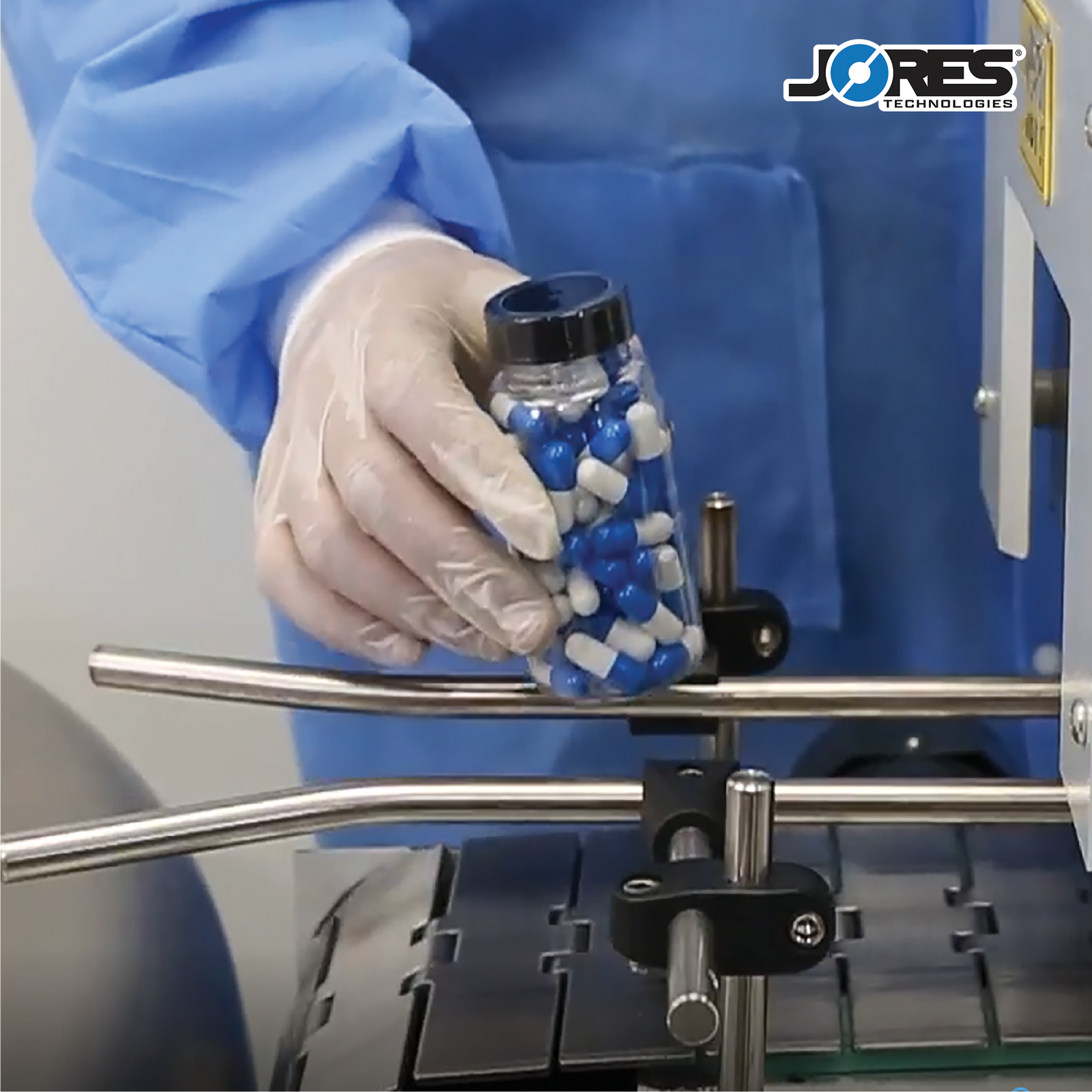 close up of a person feeding a clear container with blue and white pills into a tamper evident shrinking tunnel