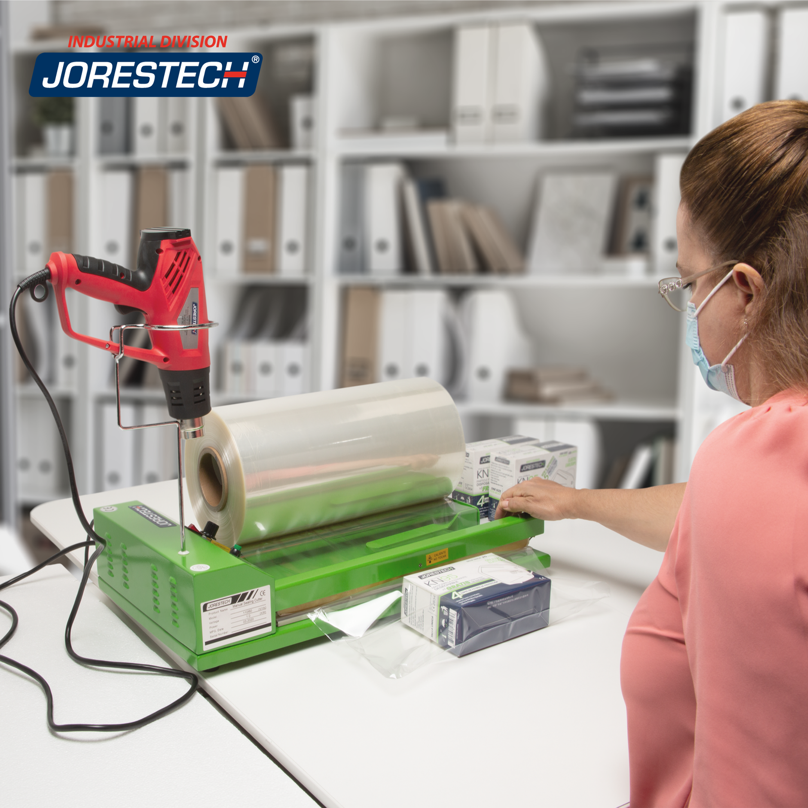 A woman in a pink shirt is using her shrink packaging unit to seal boxes of face masks. A shrink heat gun is mounted on the shrink gun holder, a roll of film rests on the roll holder bars of the 12 inch shrink film sealer dispenser