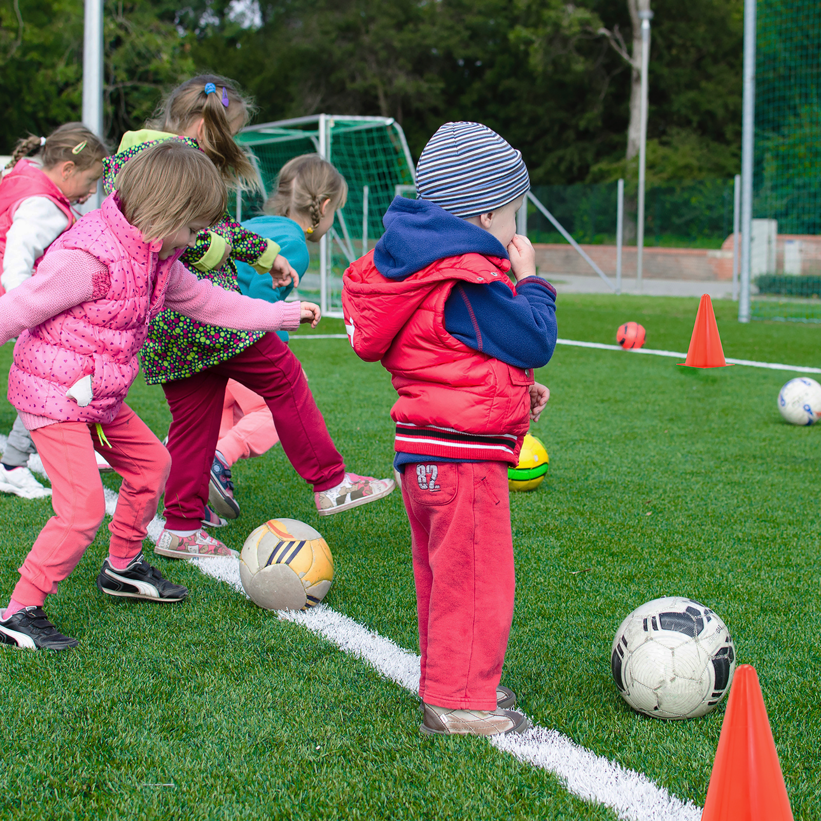 A group of kids playing in a field marked with several orange sport training cones