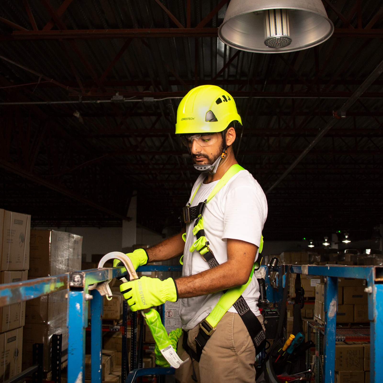 A man wearing the JORESTECH 1D fall protection safety body harness while he is attaching a shock absorbing hook of a lanyard to the metal structure of the lift where he is standing
