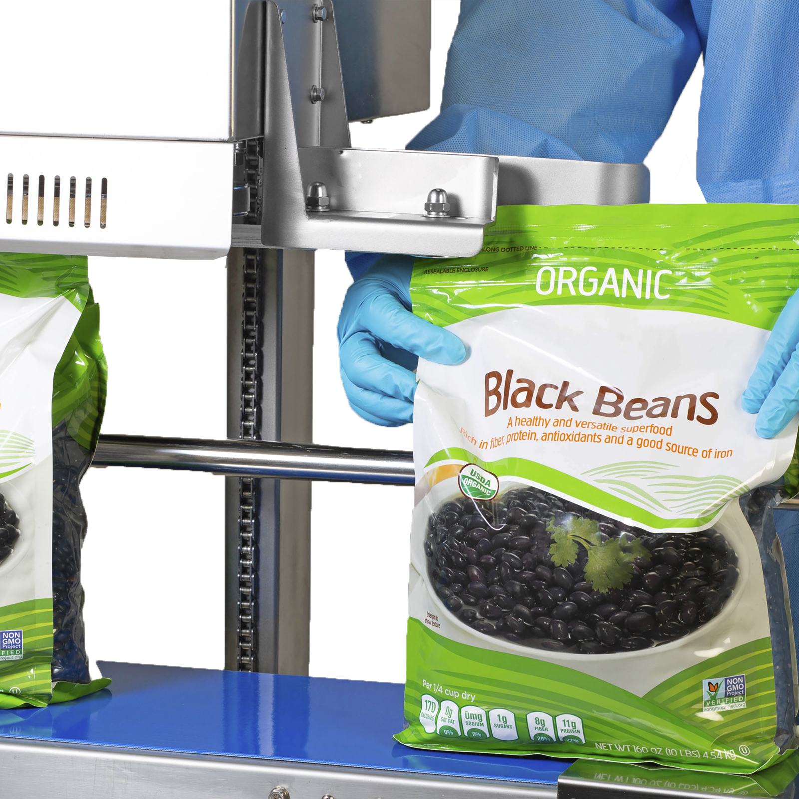 Operator wearing disposable blue clothing sealing and coding 10 pound large plastic bags filled with black beans with a vertical JORES TECHNOLOGIES® continuous band sealer for sealing vertically 