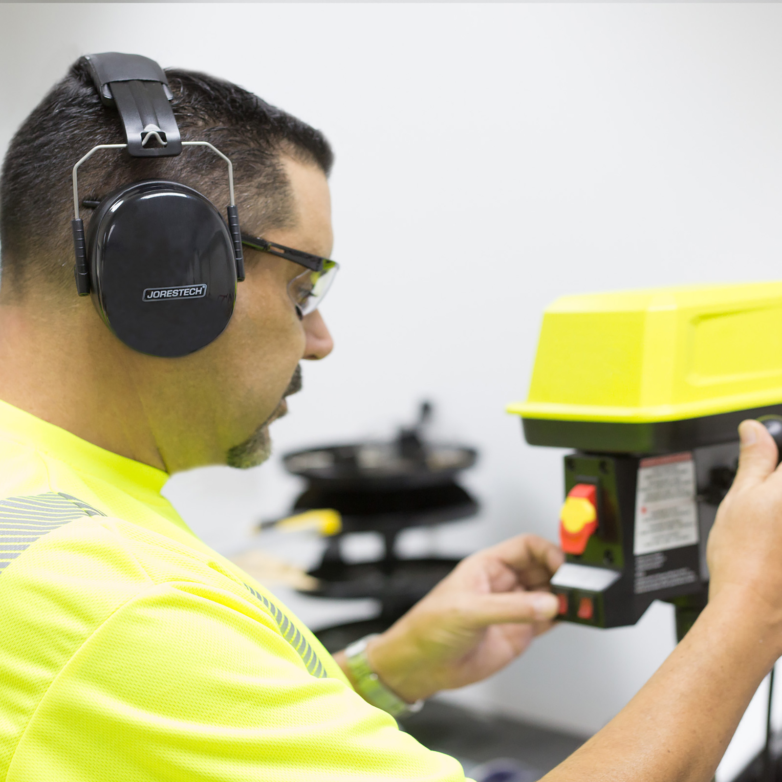 A technician wearing black ear muffs and protective eye wear while servicing a machine