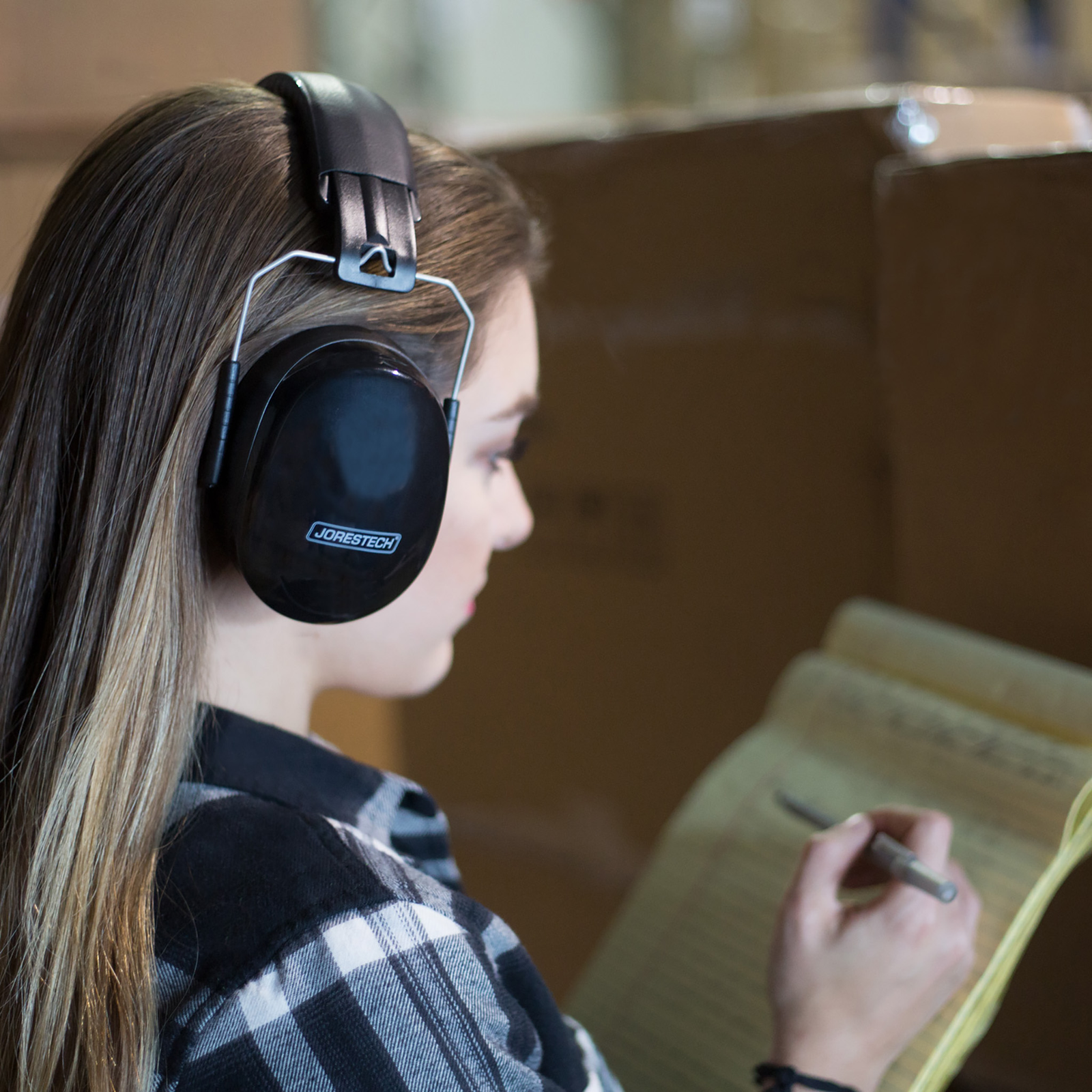 A lady wearing black ear muffs while she is taking notes of a delivery in a storage building