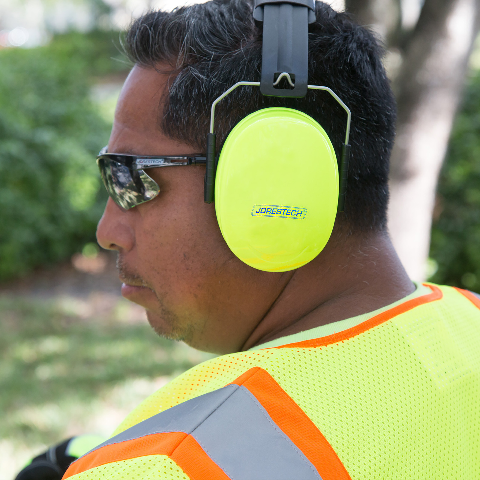 A worker wearing ear muffs over sunglasses in a setting outdoors