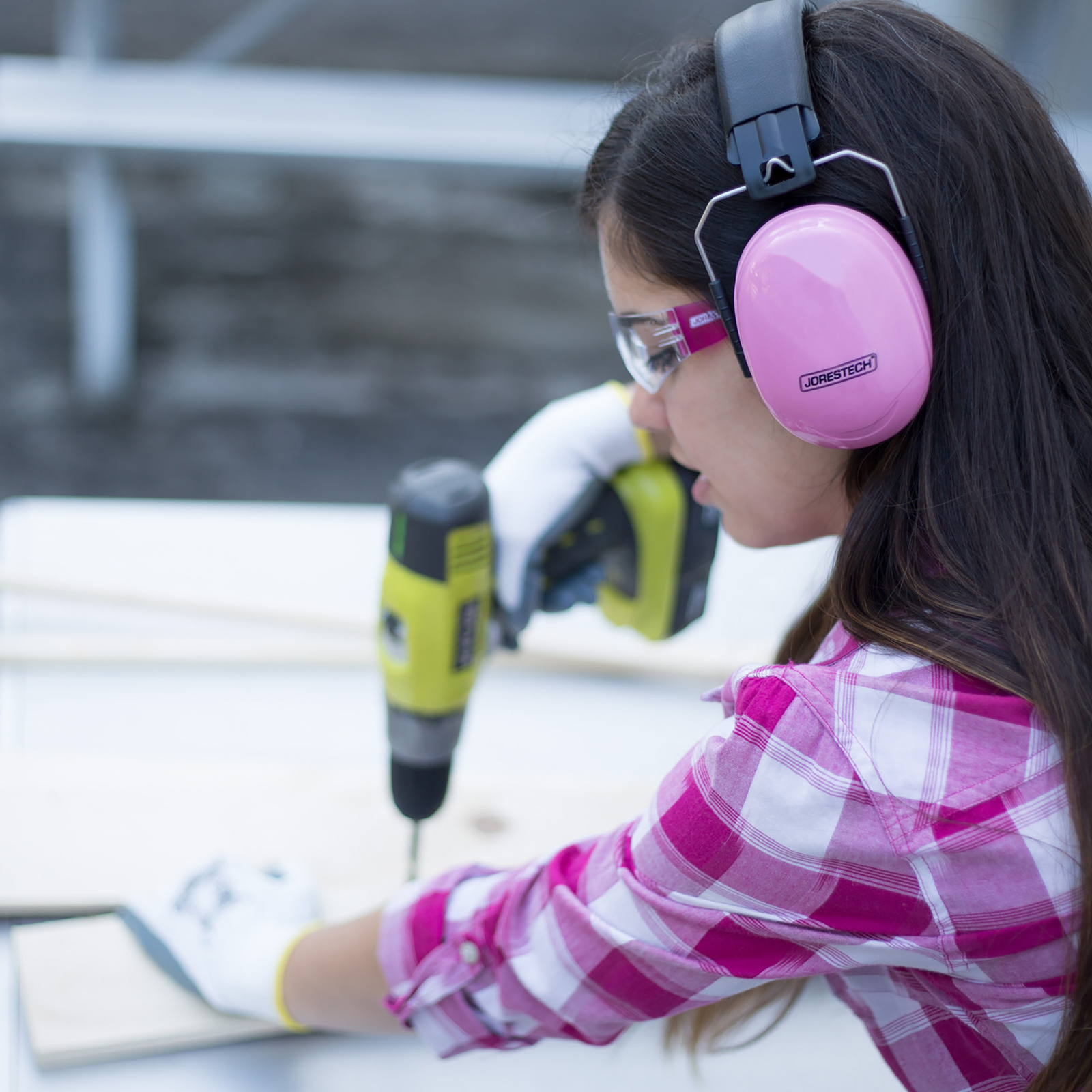 A lady wearing pink JORESTECH ear muffs for noise canceling while she is using loud power tools