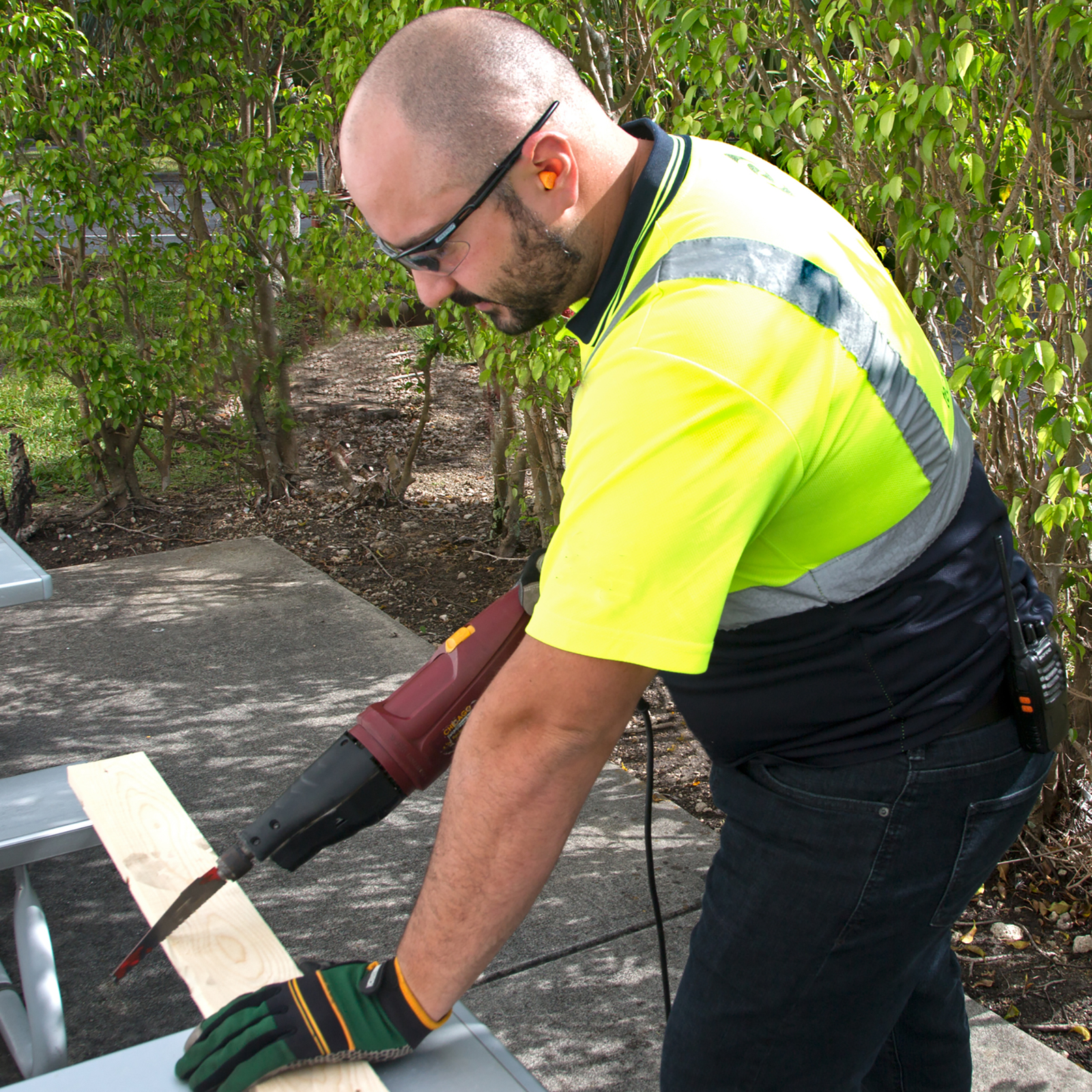 Show a worker wearing JORESTECH ear plugs while operating a loud power tool to prepare construction material.