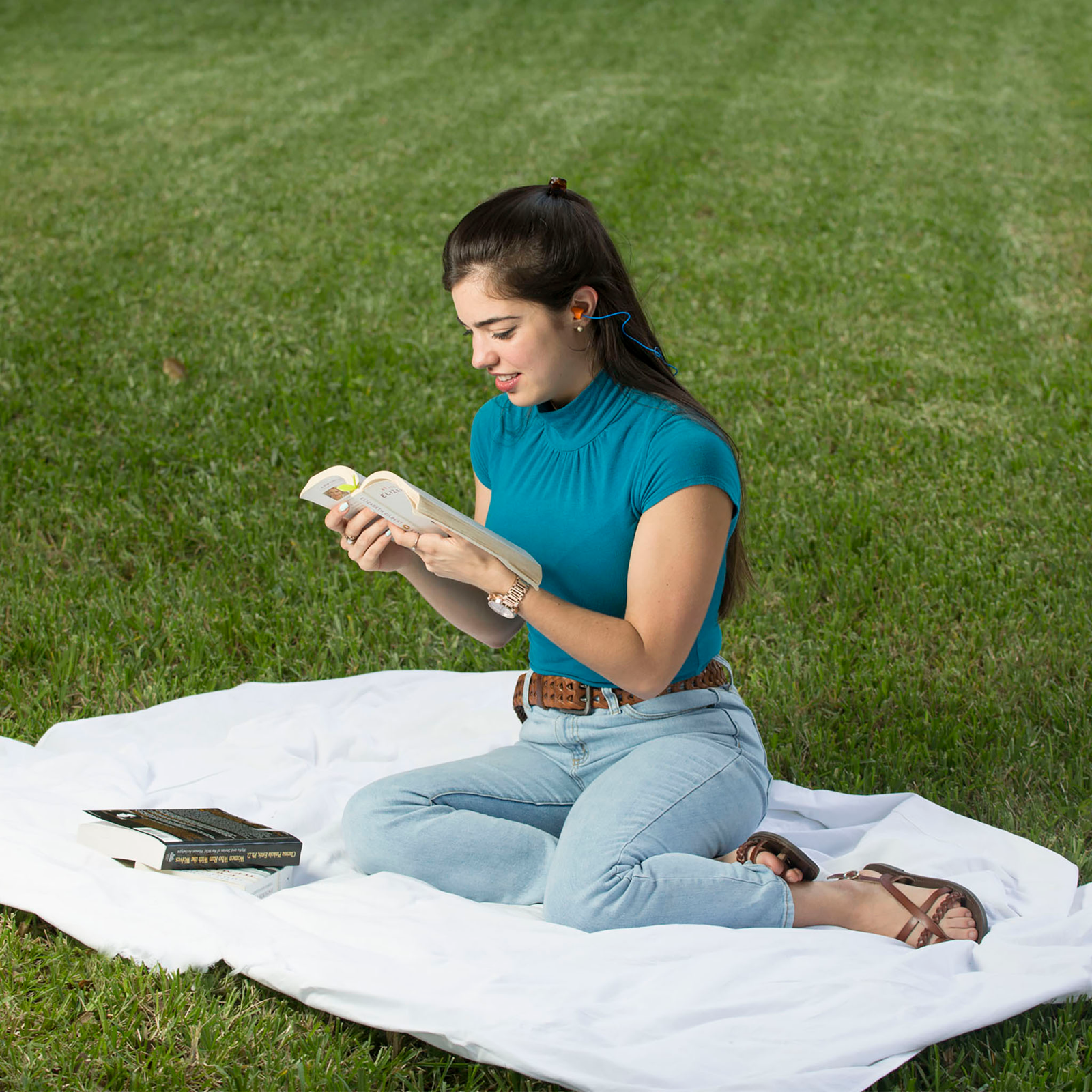 A lady wearing ear plugs for noise reduction while reading in a park