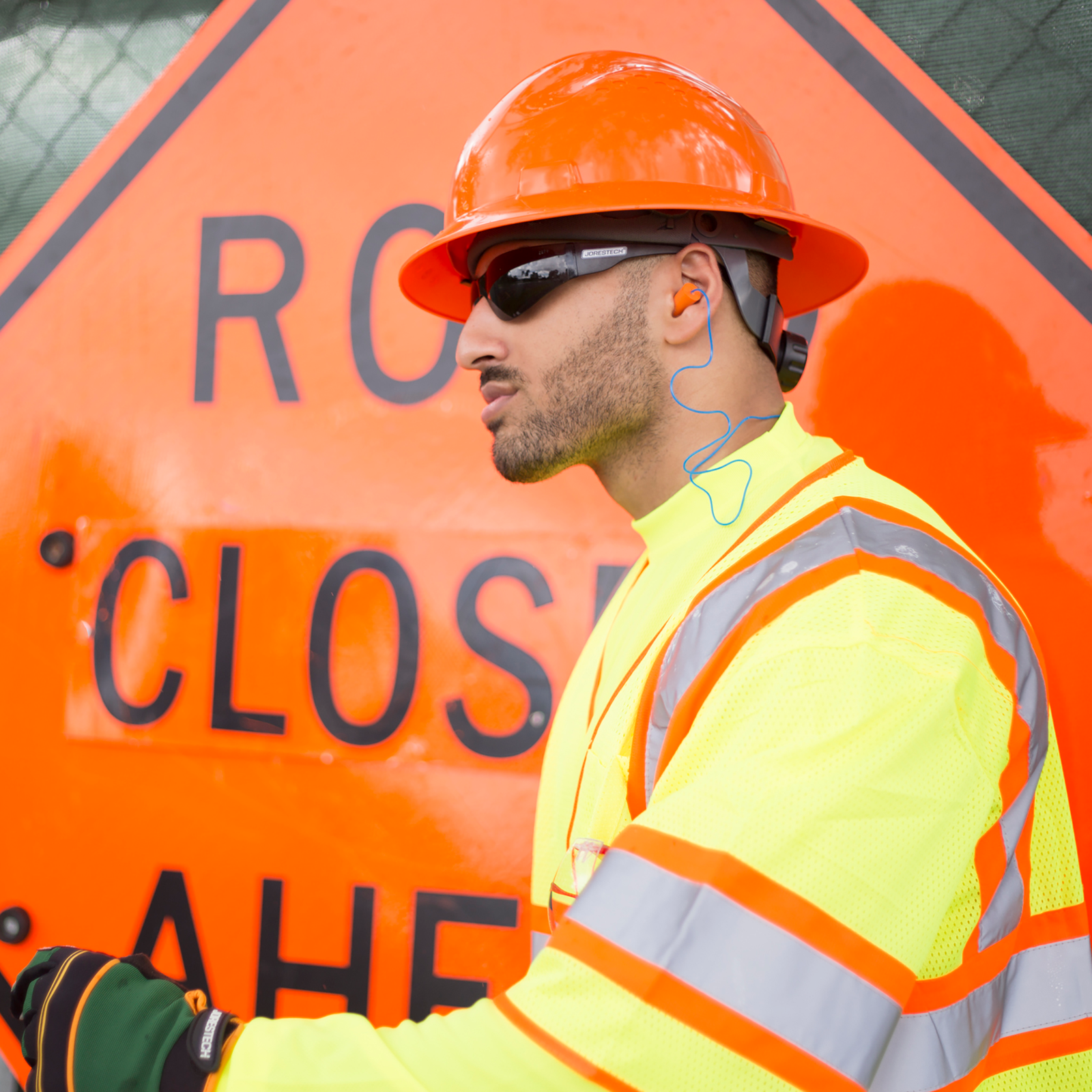 A worker wearing ear plugs for hearing protection and high visibility clothing and hard hat during a road construction