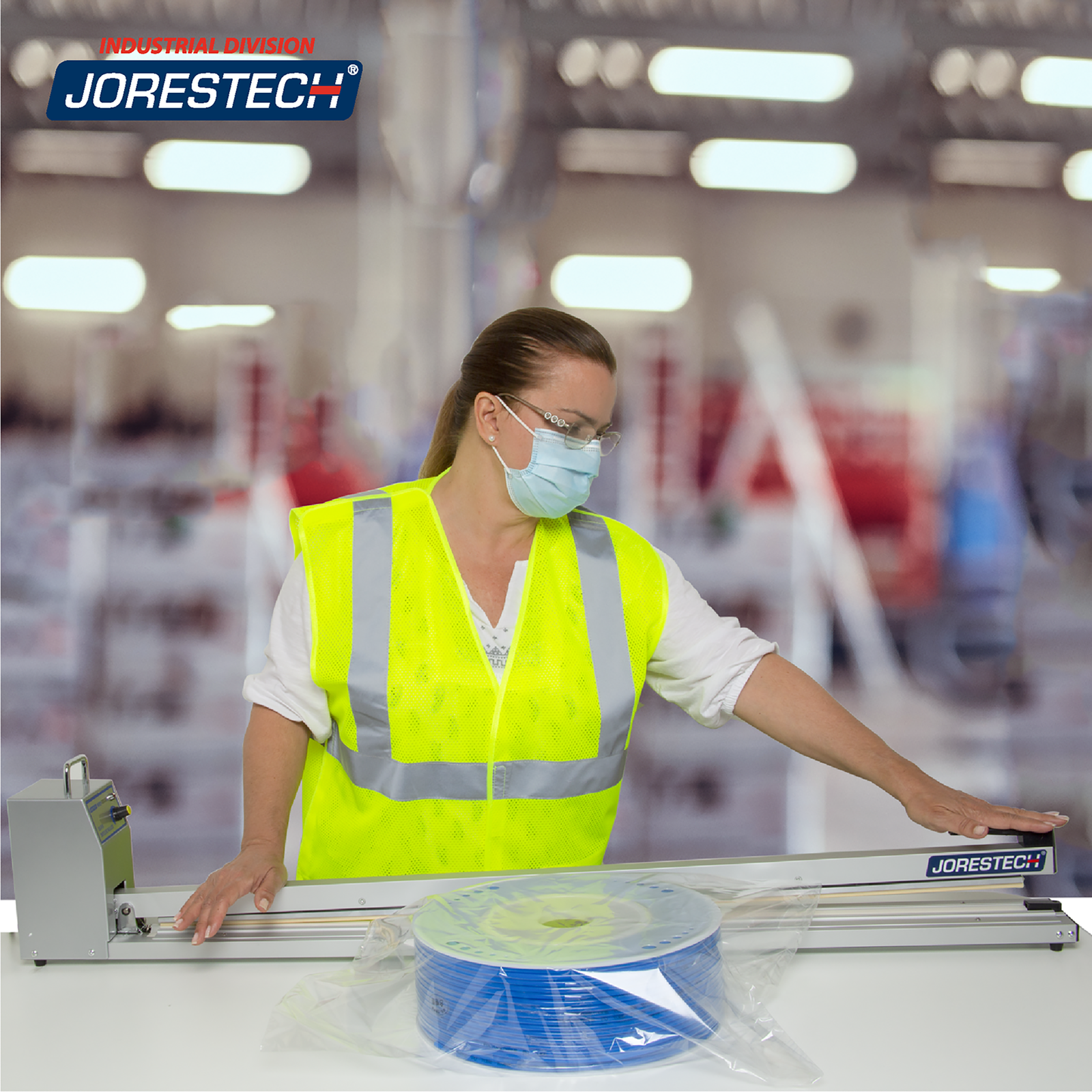 Woman in a factory setting wearing PPE sealing a bag containing a large roll of blue cable with a JORESTECH Extra Long Manual Impulse Bag Sealer.
