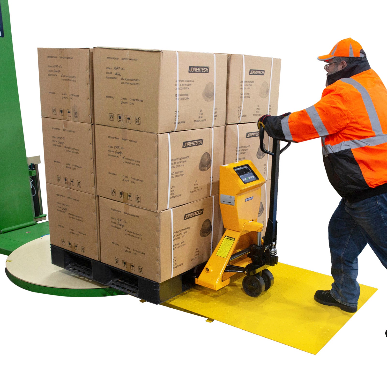 Man with a high-vis orange safety jacket setting down a pallet loaded with boxes on the pallet jack's turntable. He is stepping on the loading ramp and part of the pallet jack is rolling off the loading ramp as well.