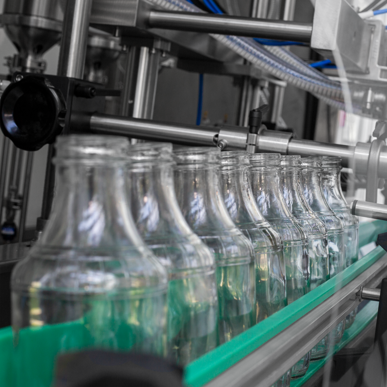 closeup of several clear glass containers which are set on the conveyor belt of the jorestech 6 head inline piston filler