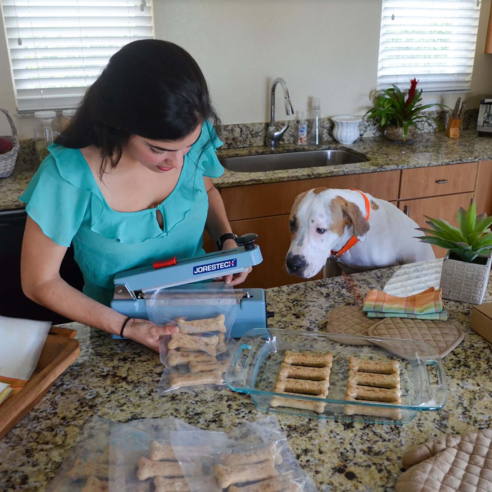 Woman and her dog in their kitchen. she is packaging Dog treats in sealable bags with the JORES TECHNOLOGIES® 8 inch manual impulse sealer.