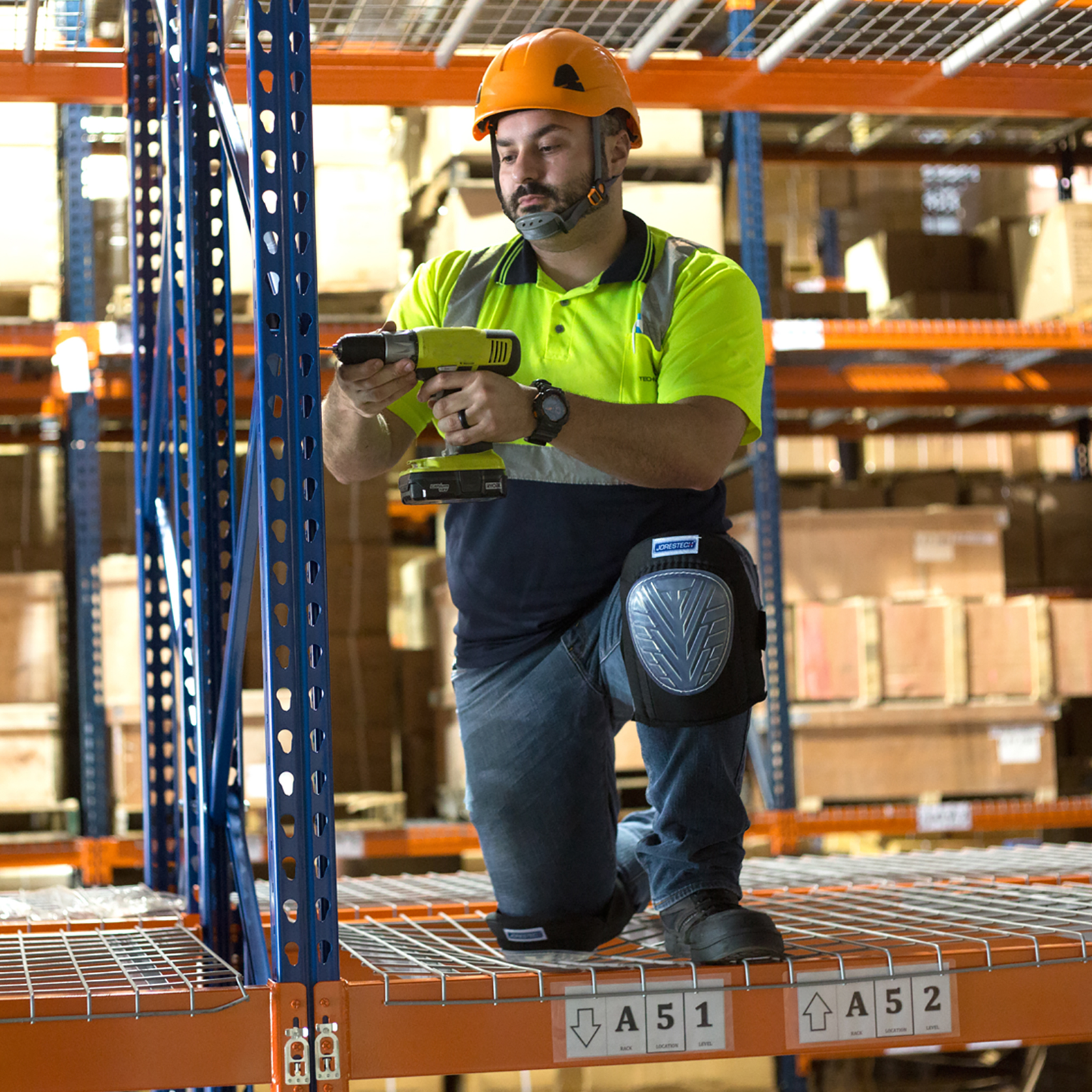 A worker kneeling on top of a grid while installing the racks of a warehouse using the JORESTECH anti skid knee pads