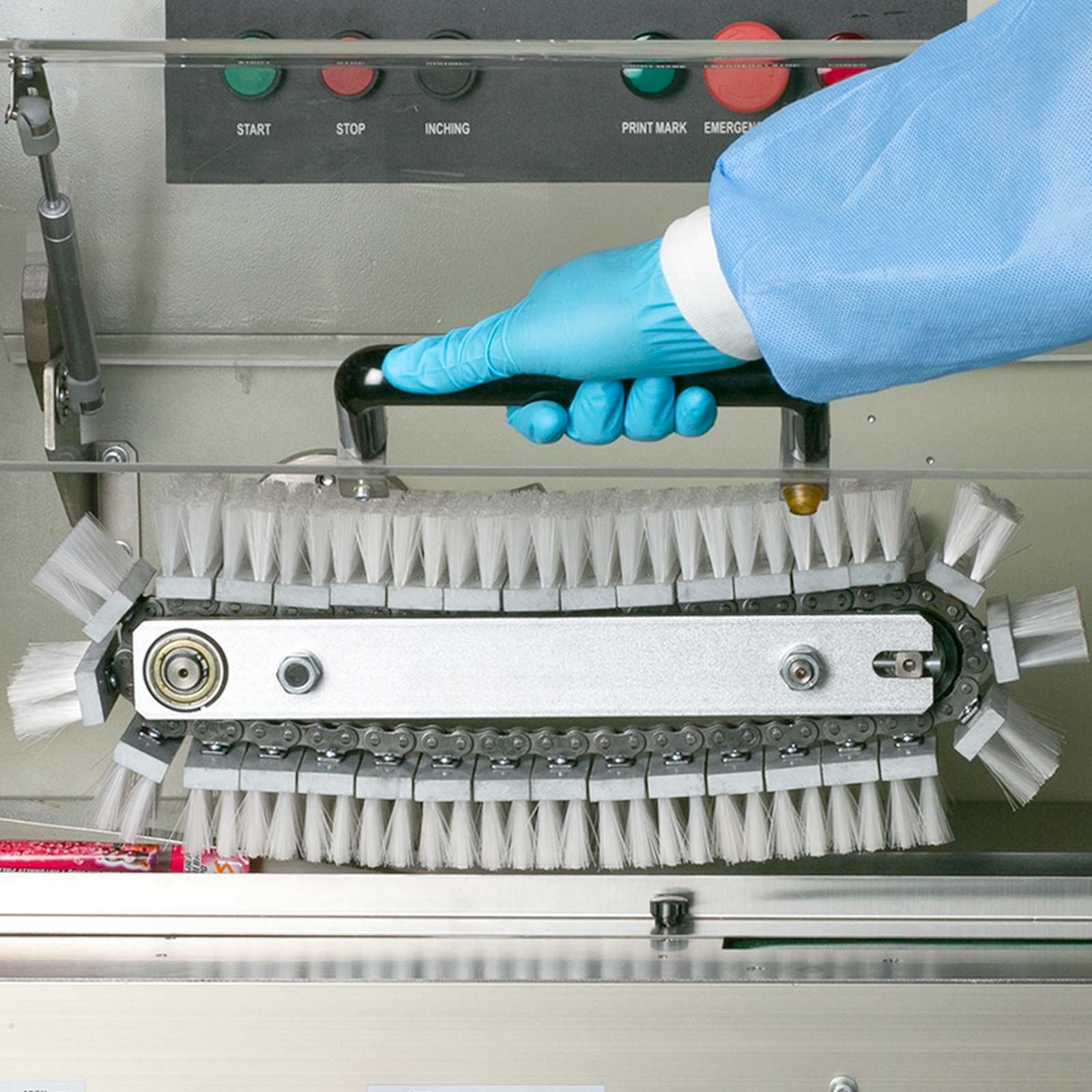 Close up shot of the internal parts on a JORESTECH® Flow packaging machine and the hand of a person opening a clear door to inspect the sweeping brushes 