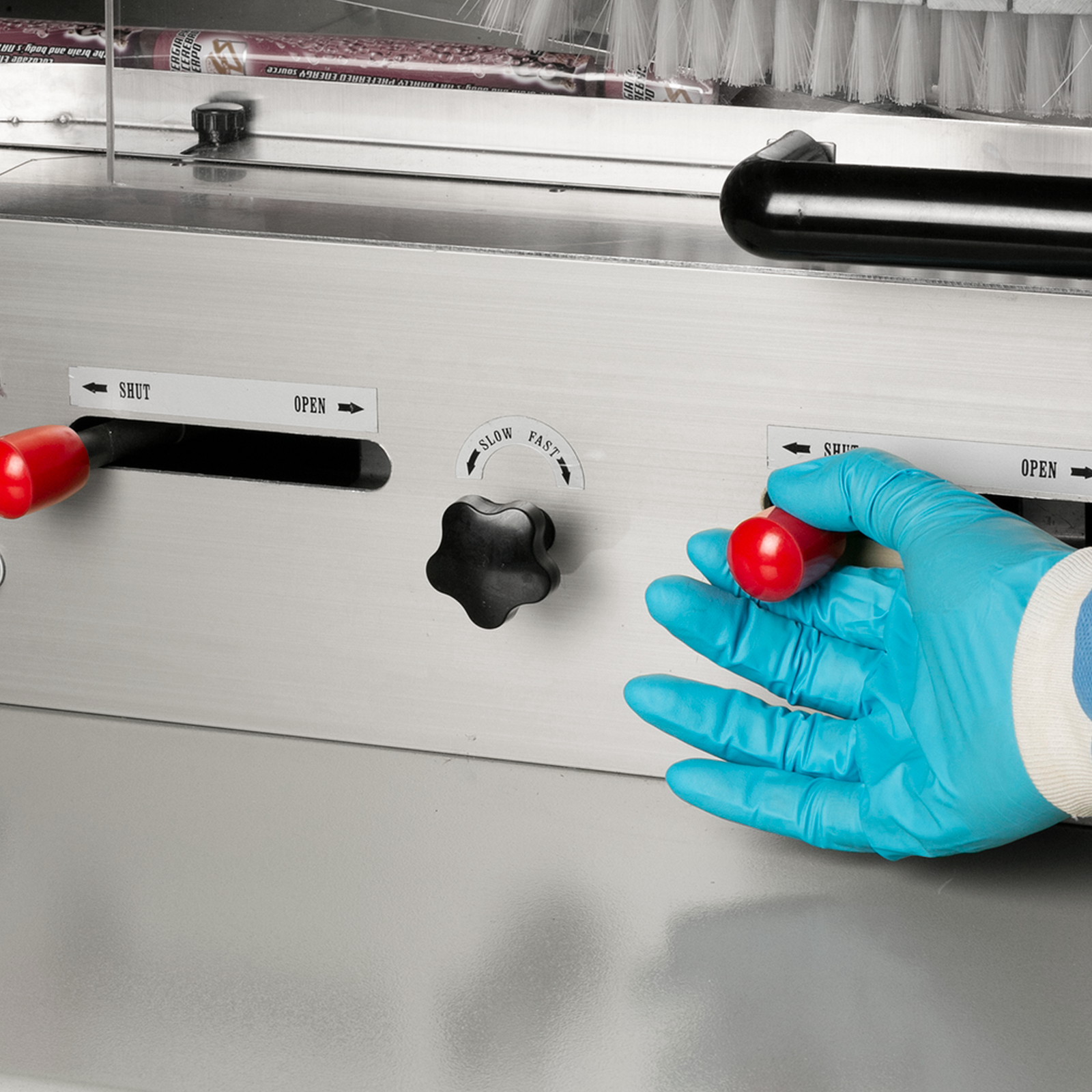 Close-up shot of an operator wearing a blue PPE glove operating a horizontal flow pack machine